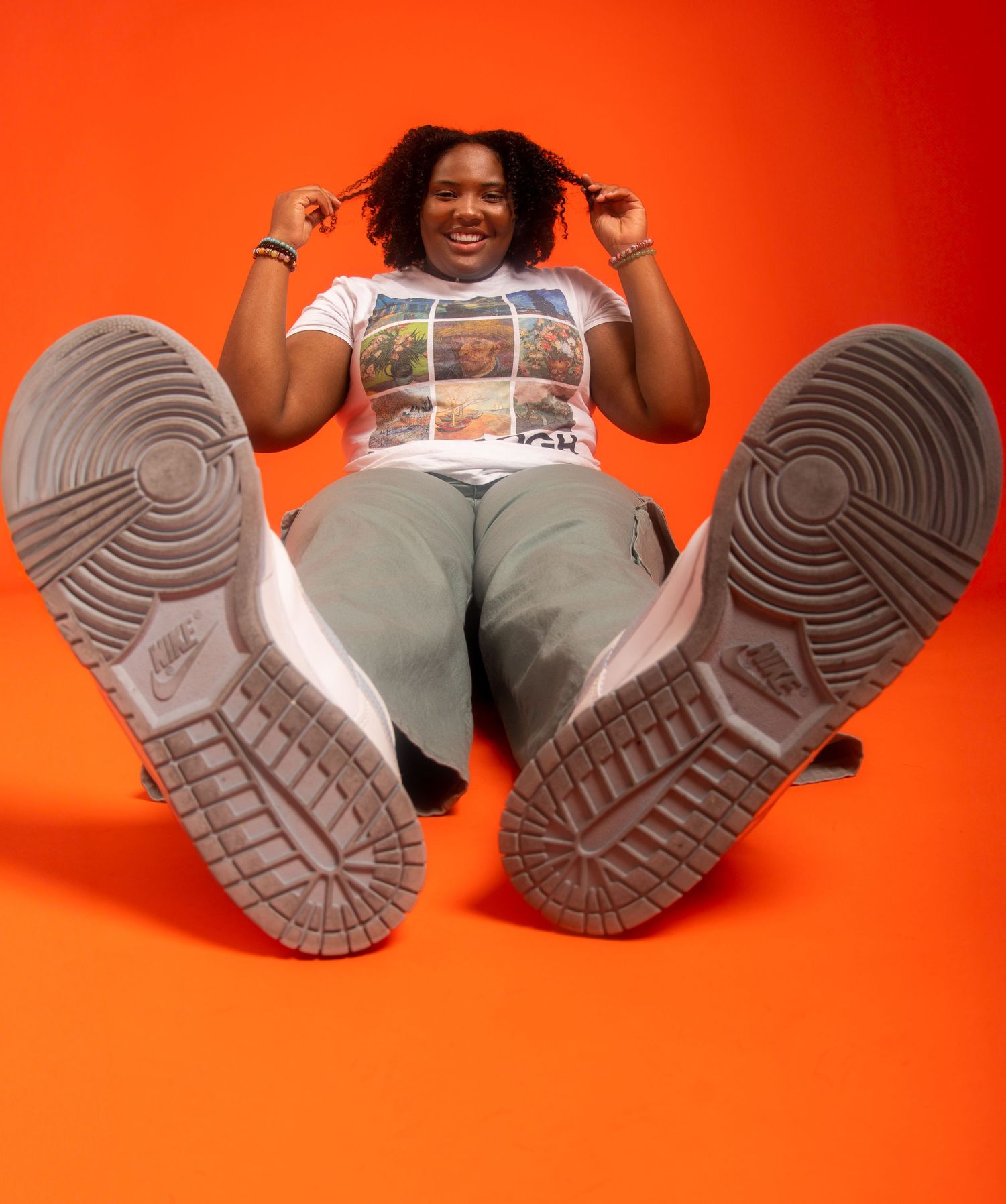 Person in white shirt and olive pants sits on orange background showing the soles of their work boots.