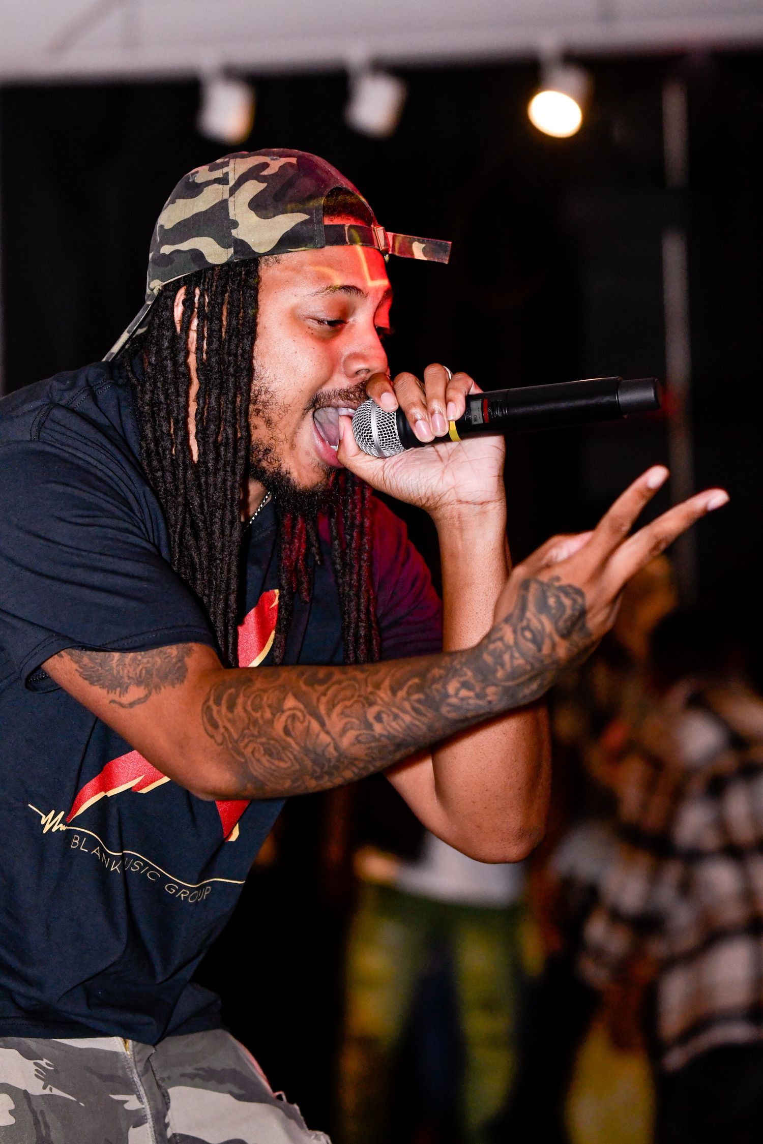 Performer with dreadlocks and tattoos energetically rapping into a microphone on stage during a concert performance.