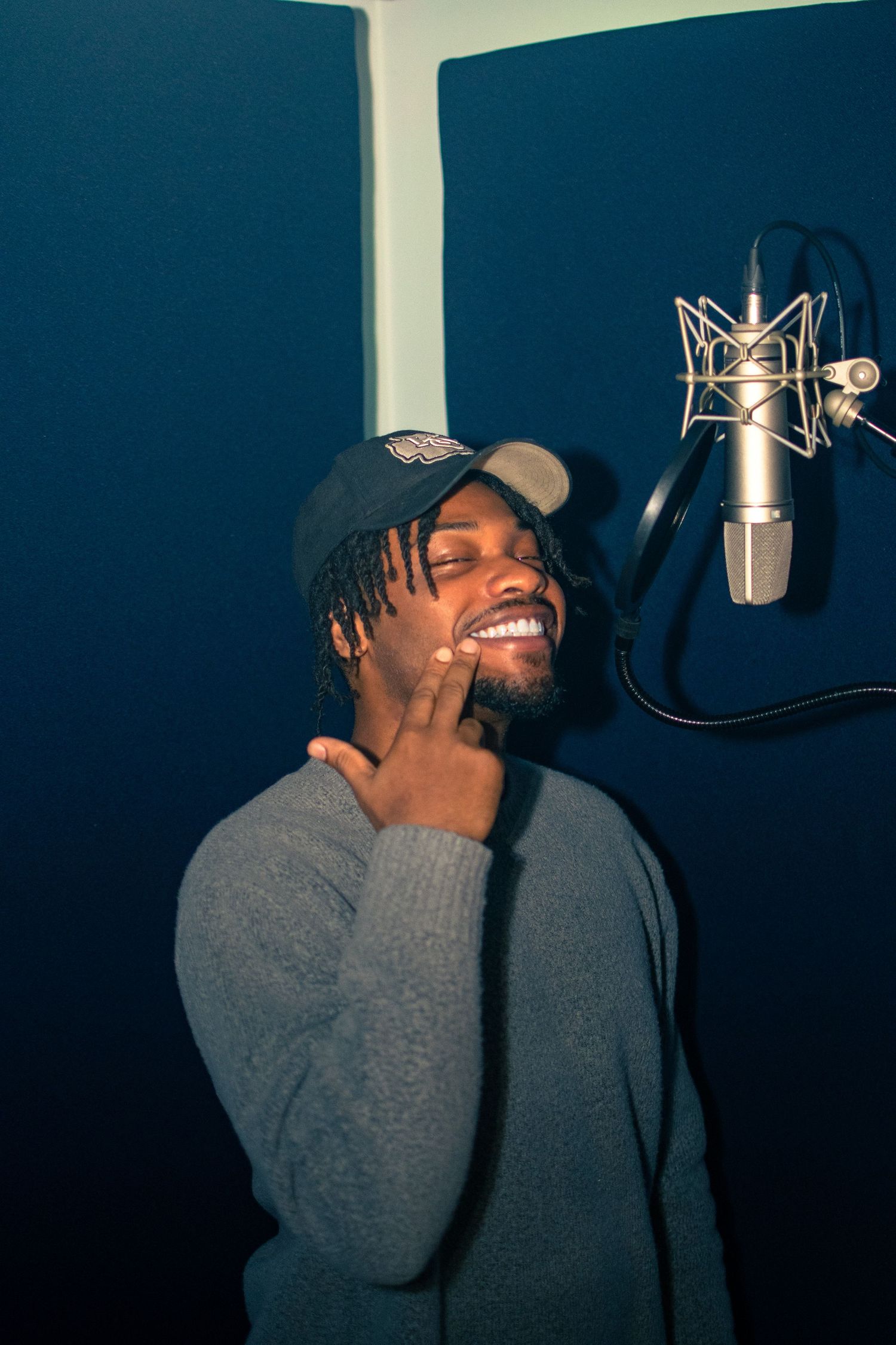 A series of four studio recording photos showing someone in a gray sweater laughing while recording vocals.