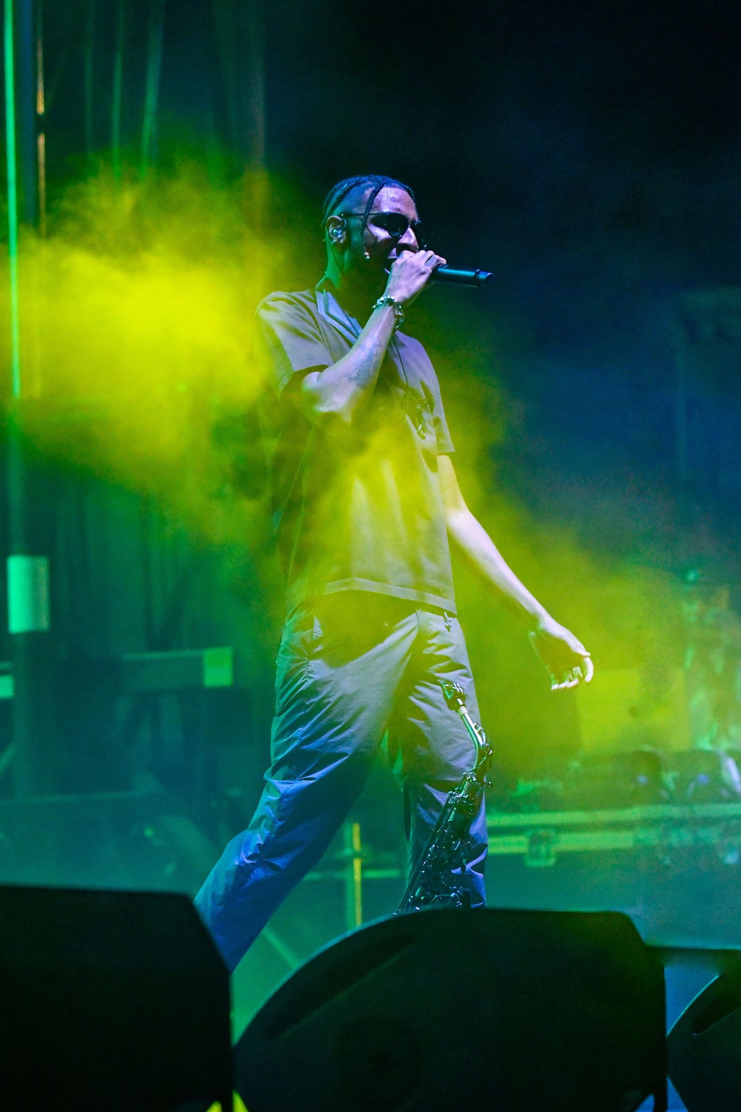 Performer in white clothing creates dynamic movements on stage with vibrant green and blue lighting effects in background.