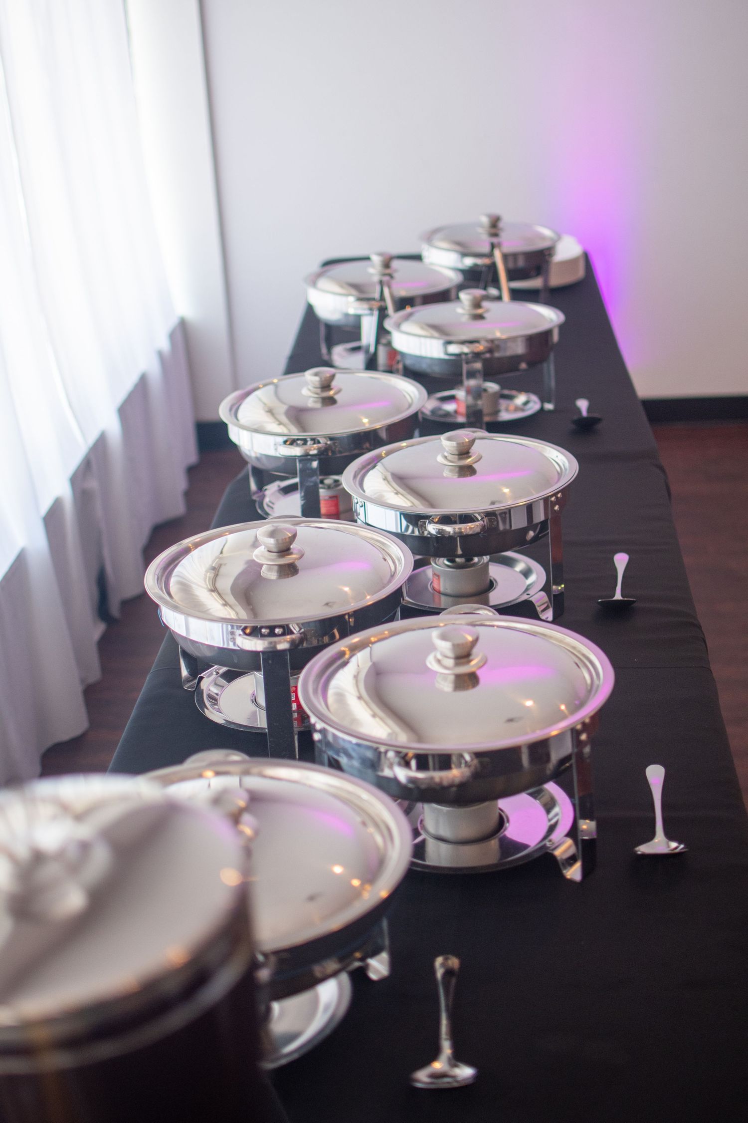 Elegant table setting with covered chafing dishes and wine glasses arranged on a dark surface.