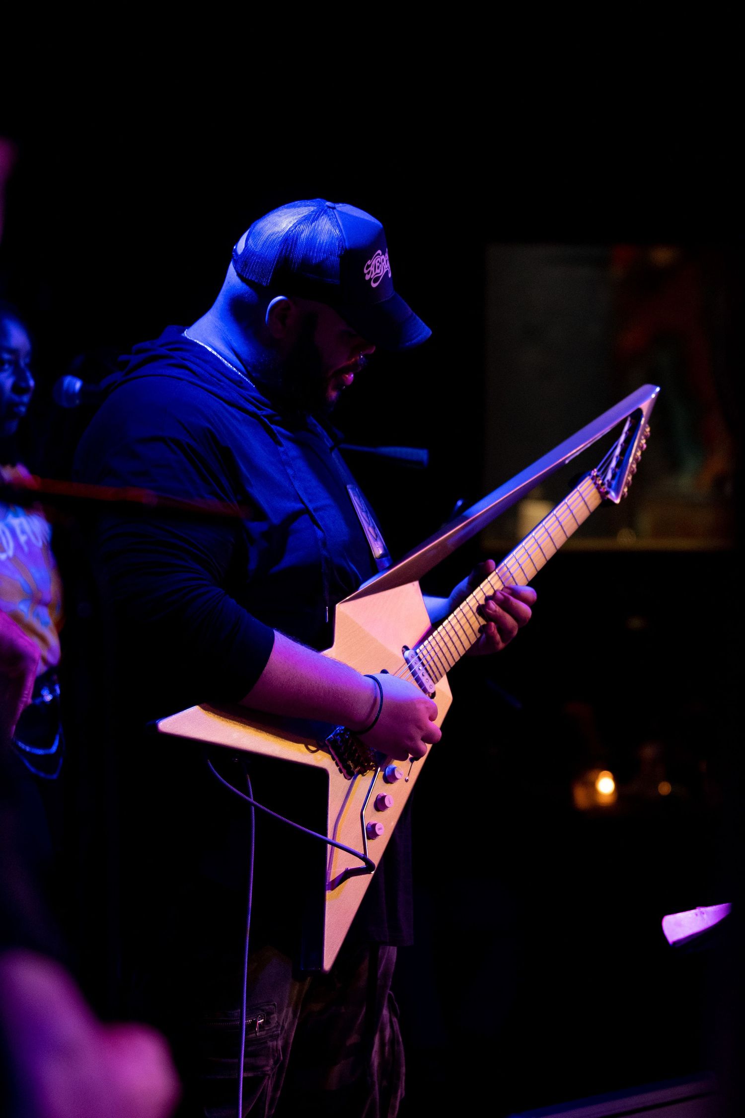Electric guitar player performs on dark stage illuminated by dramatic blue and purple lighting effects.