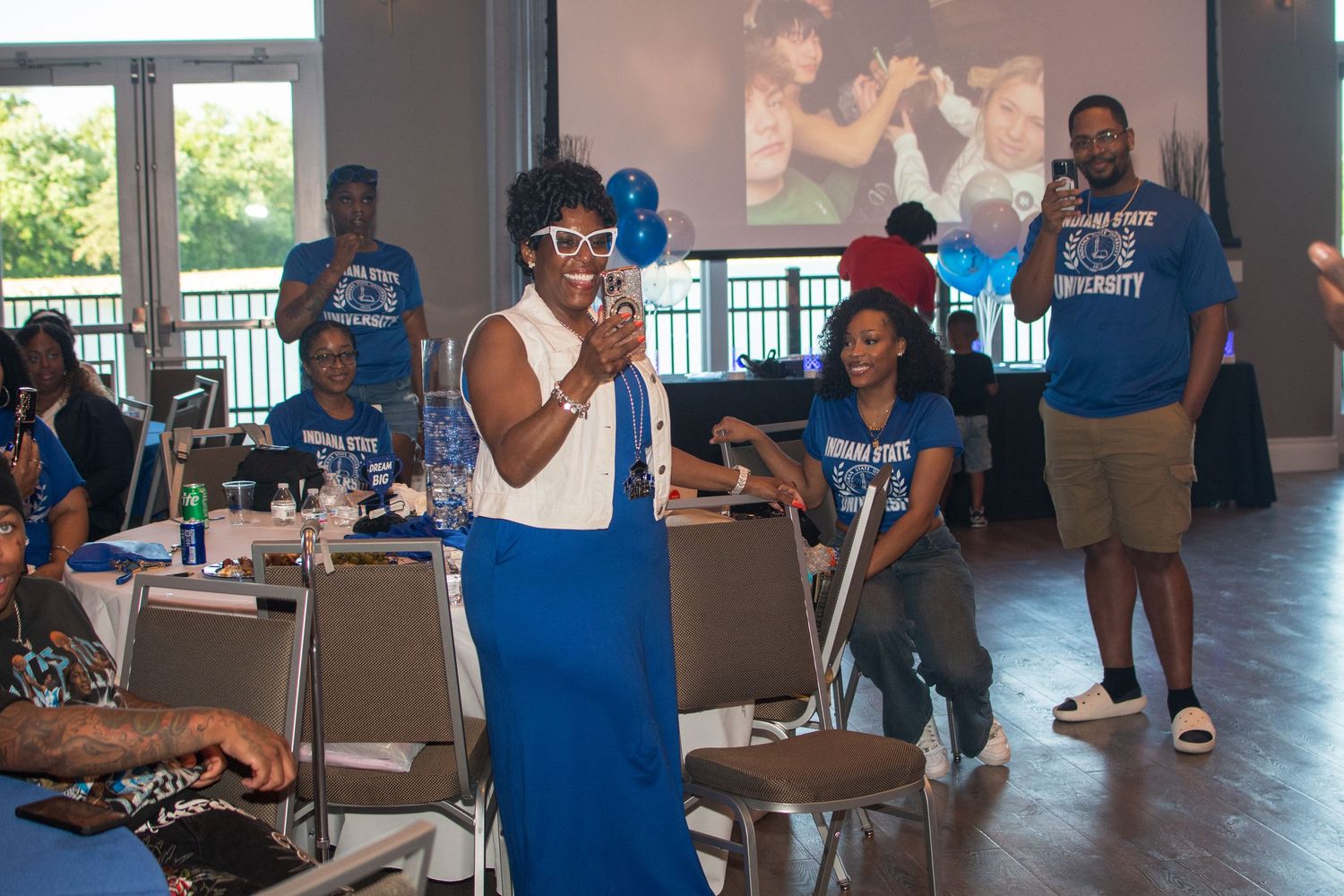 People in blue shirts gather at tables during a community event in an indoor space.