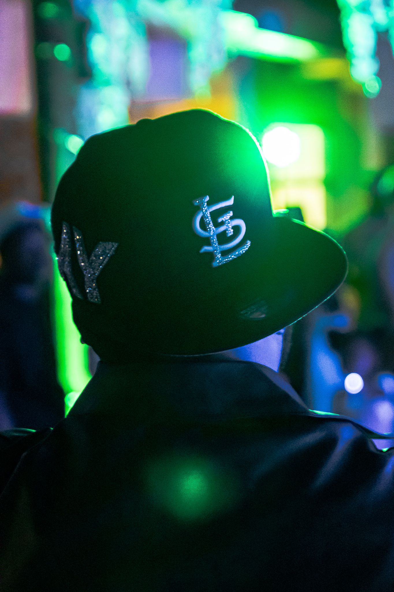 Person wearing a St. Louis Cardinals snapback cap under green neon lights at a nightclub event.