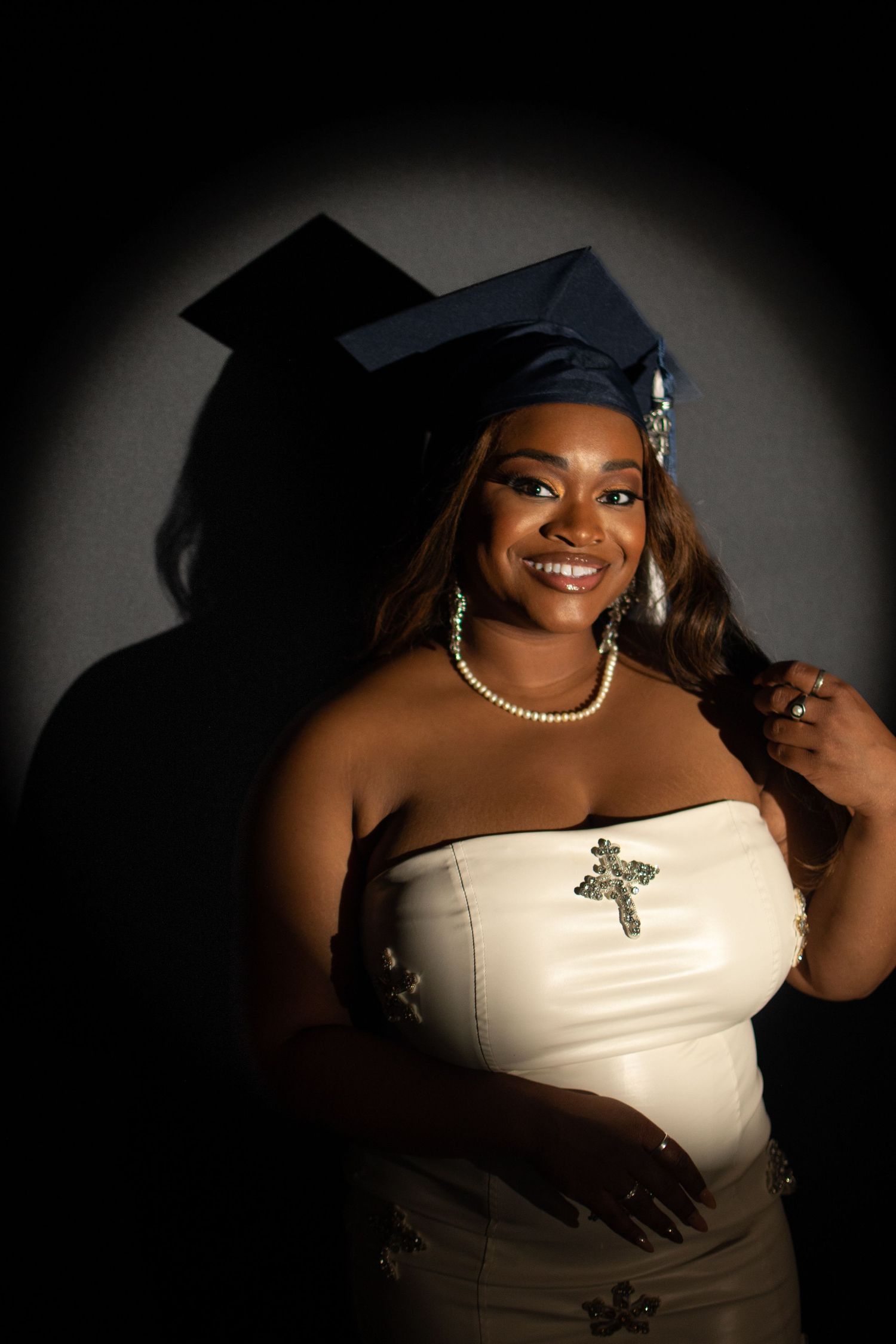 Graduation portrait featuring elegant white dress and floral crown against dramatic dark backdrop.