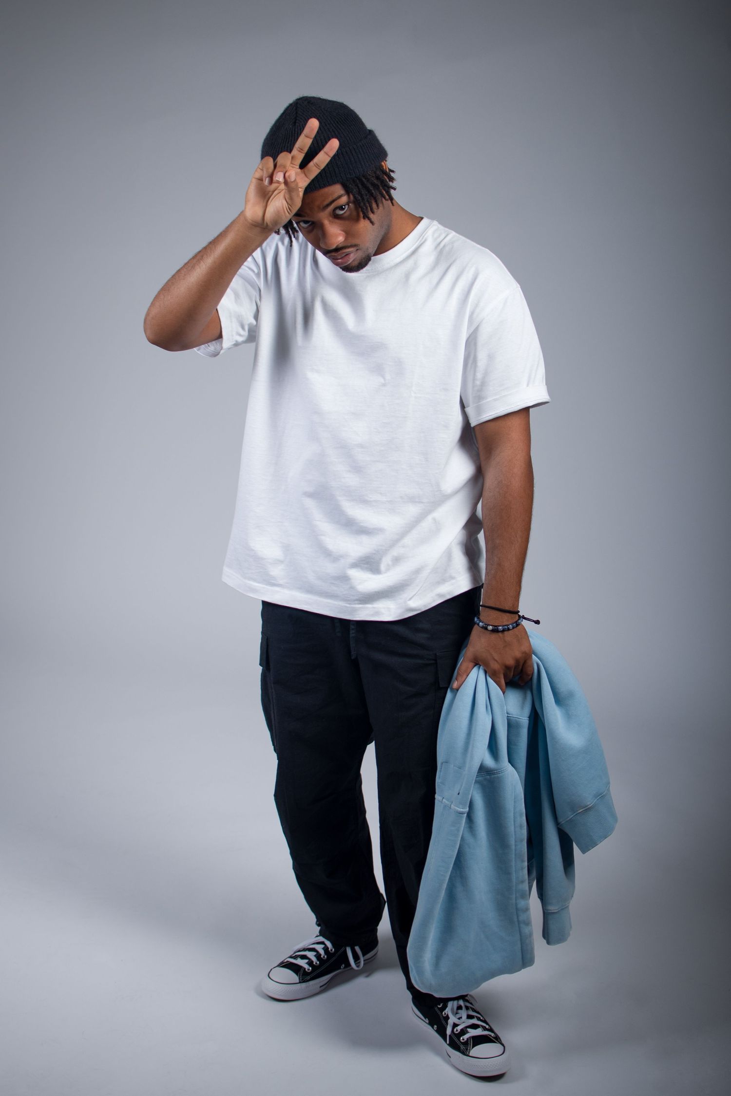 A series of fashion poses showing a person in a white t-shirt, black pants and sneakers holding a light blue jacket.