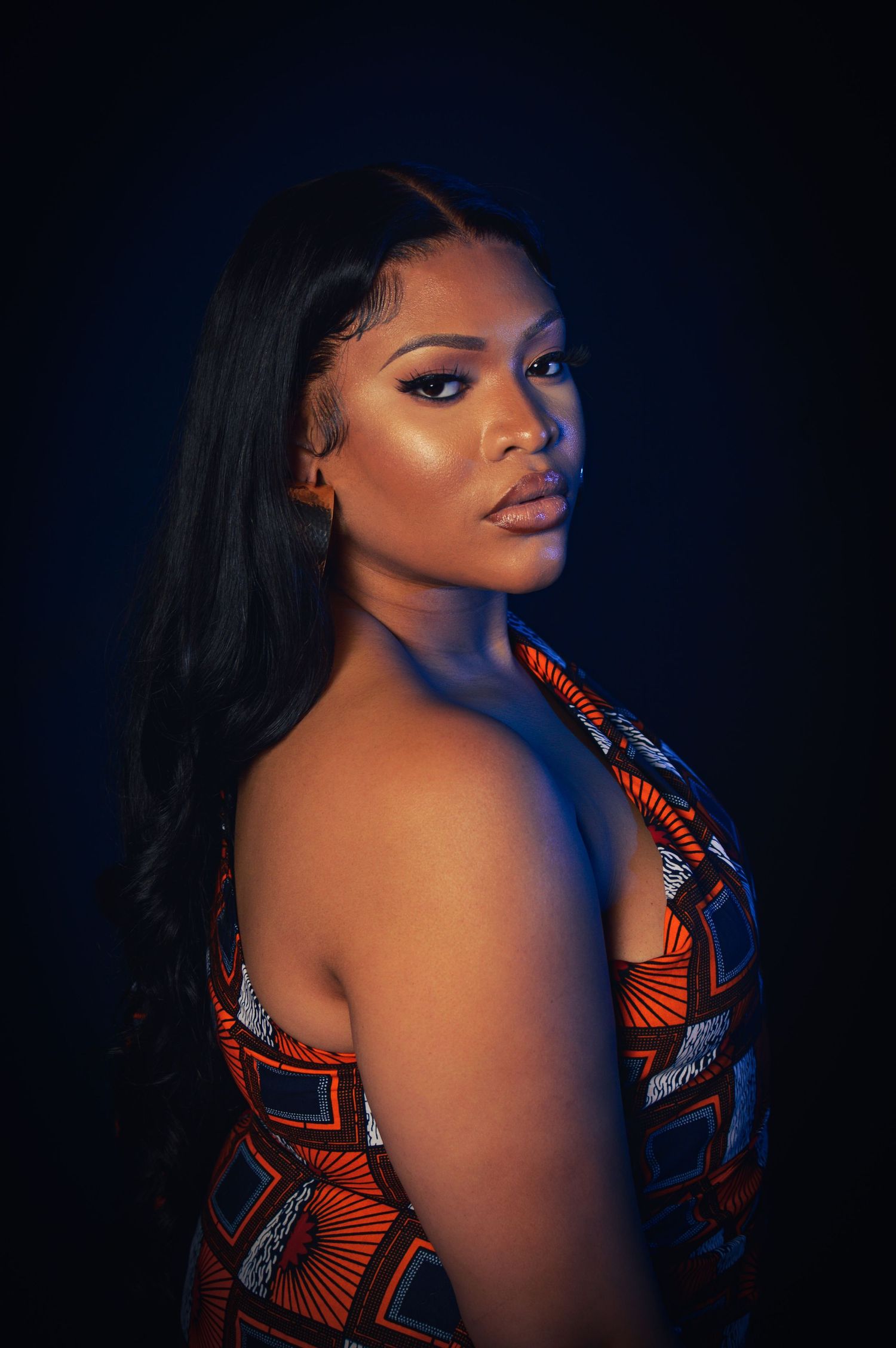 Artistic portrait series showing silhouette against dark blue background wearing vibrant orange and black patterned fabric.