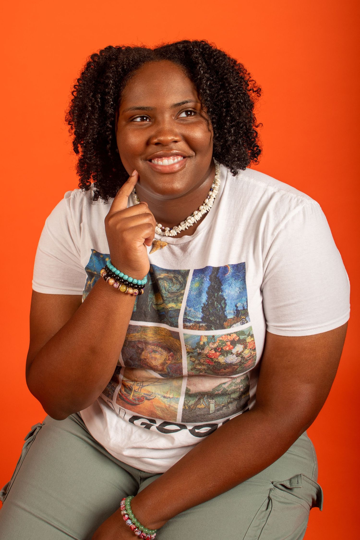 Studio portraits against vibrant orange background featuring casual white t-shirt and olive pants.