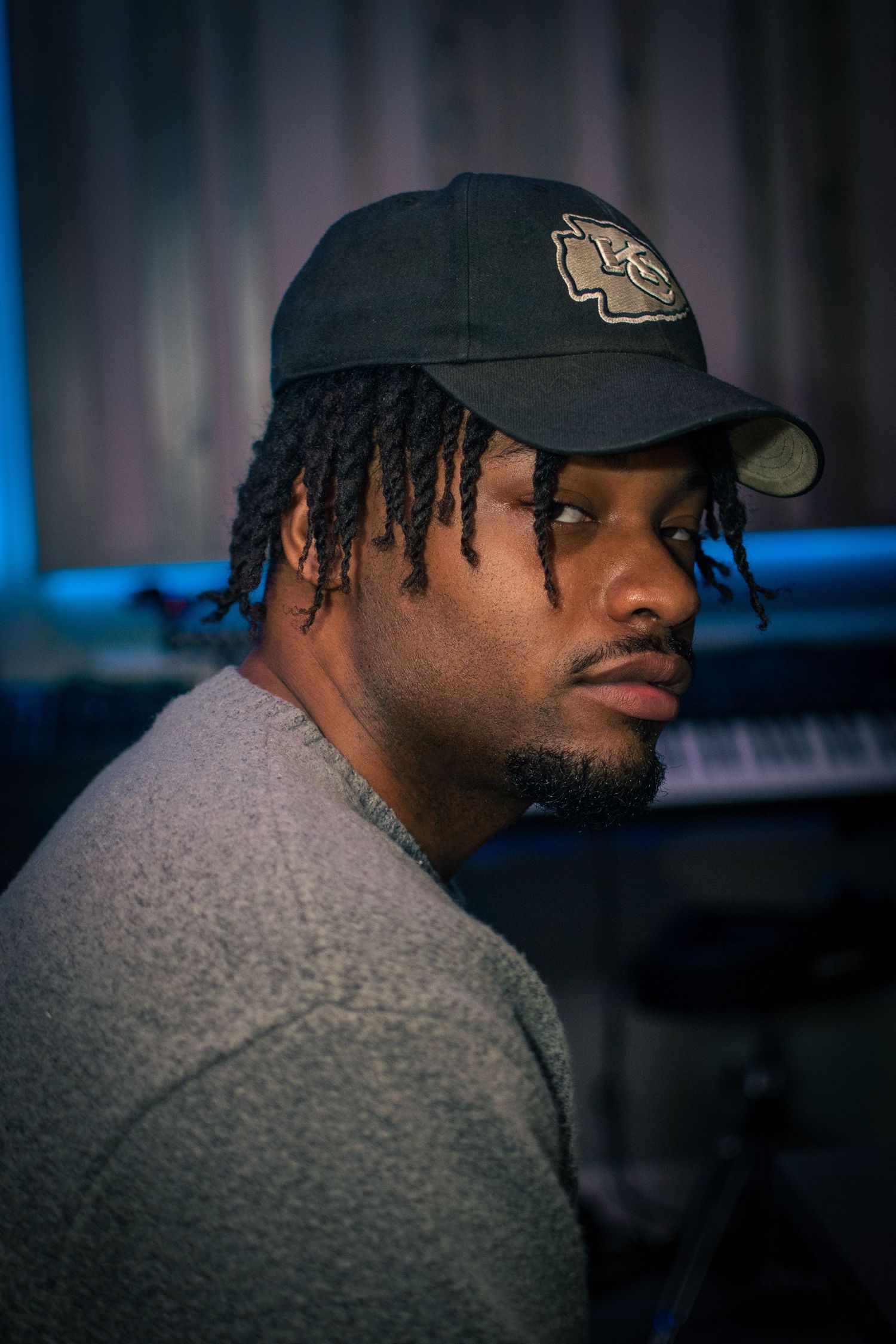 Portrait series in moody lighting showing person wearing baseball cap and grey sweater.