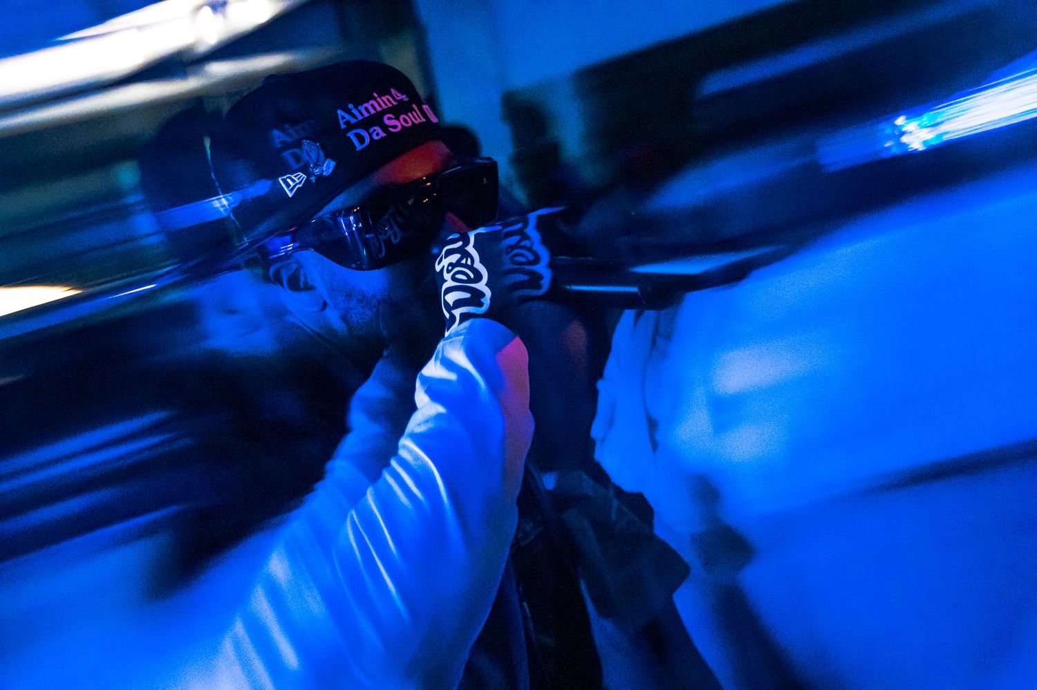 Person wearing a cap under blue UV light, holding a microphone in a dark, dramatic concert setting.