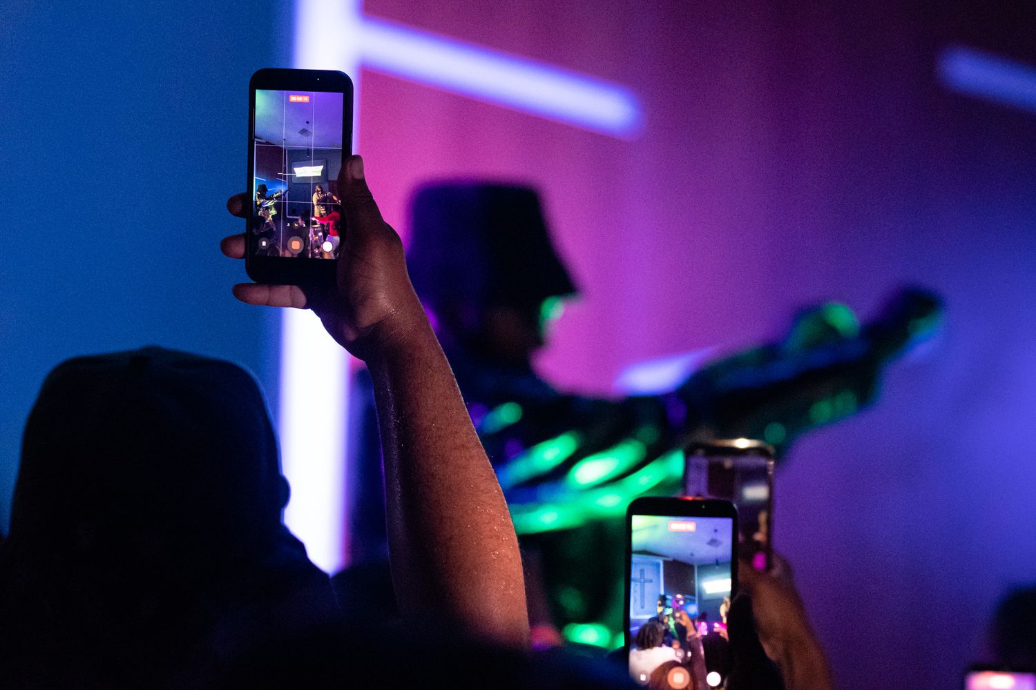 Silhouetted crowd at a nightclub with blue and purple lighting effects and raised mobile phones recording the event.
