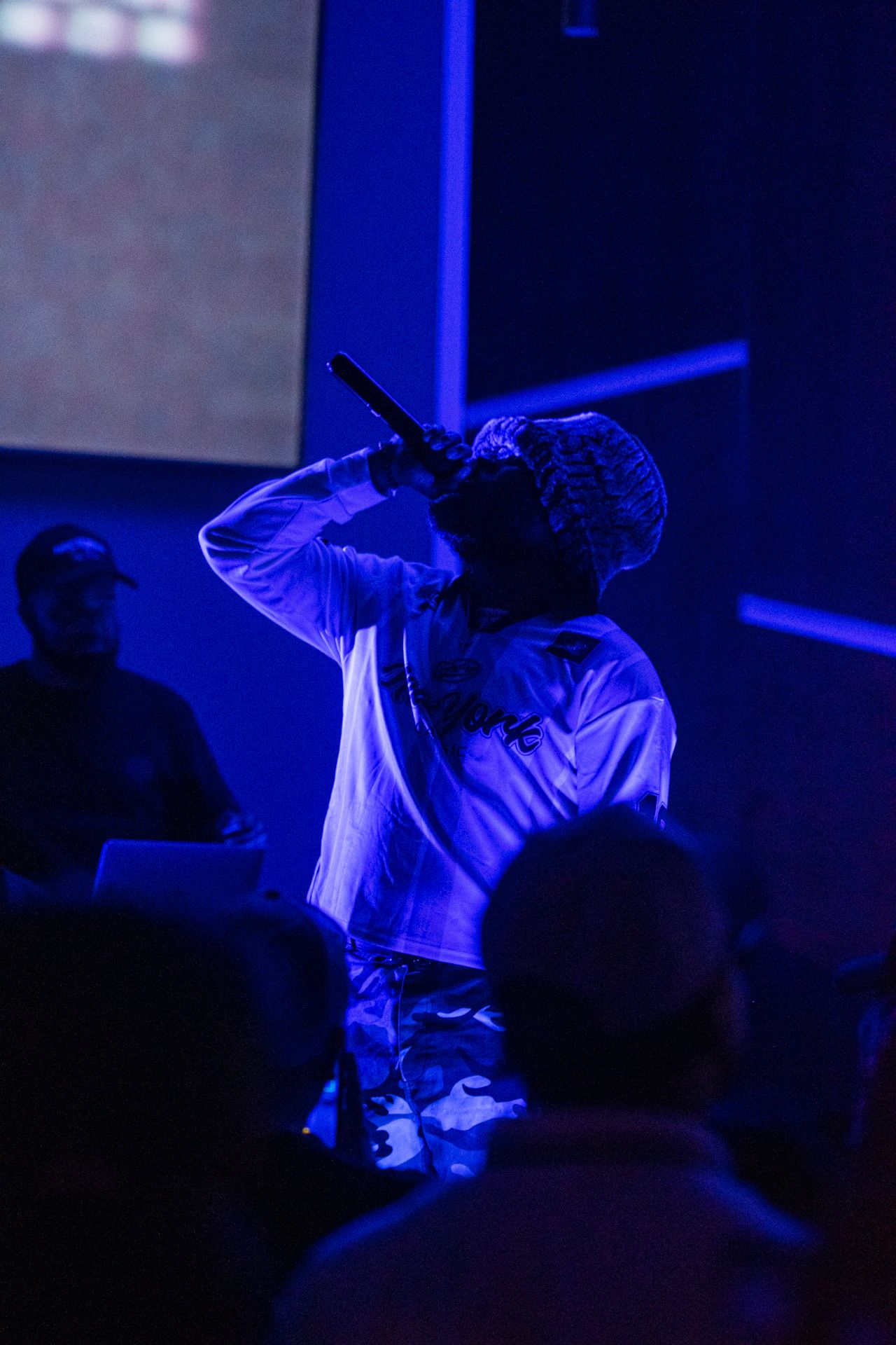 A performer silhouetted in blue stage lighting holds a microphone while singing during a live concert performance.