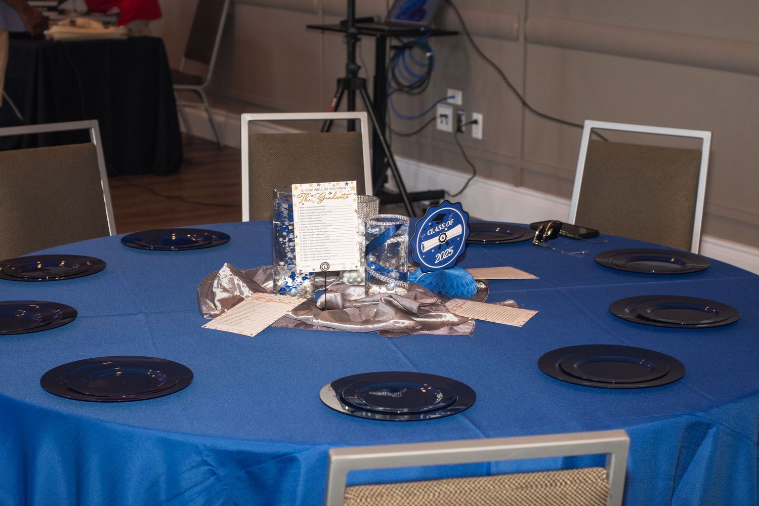 Round black plates are arranged on a blue tablecloth at an event setting.