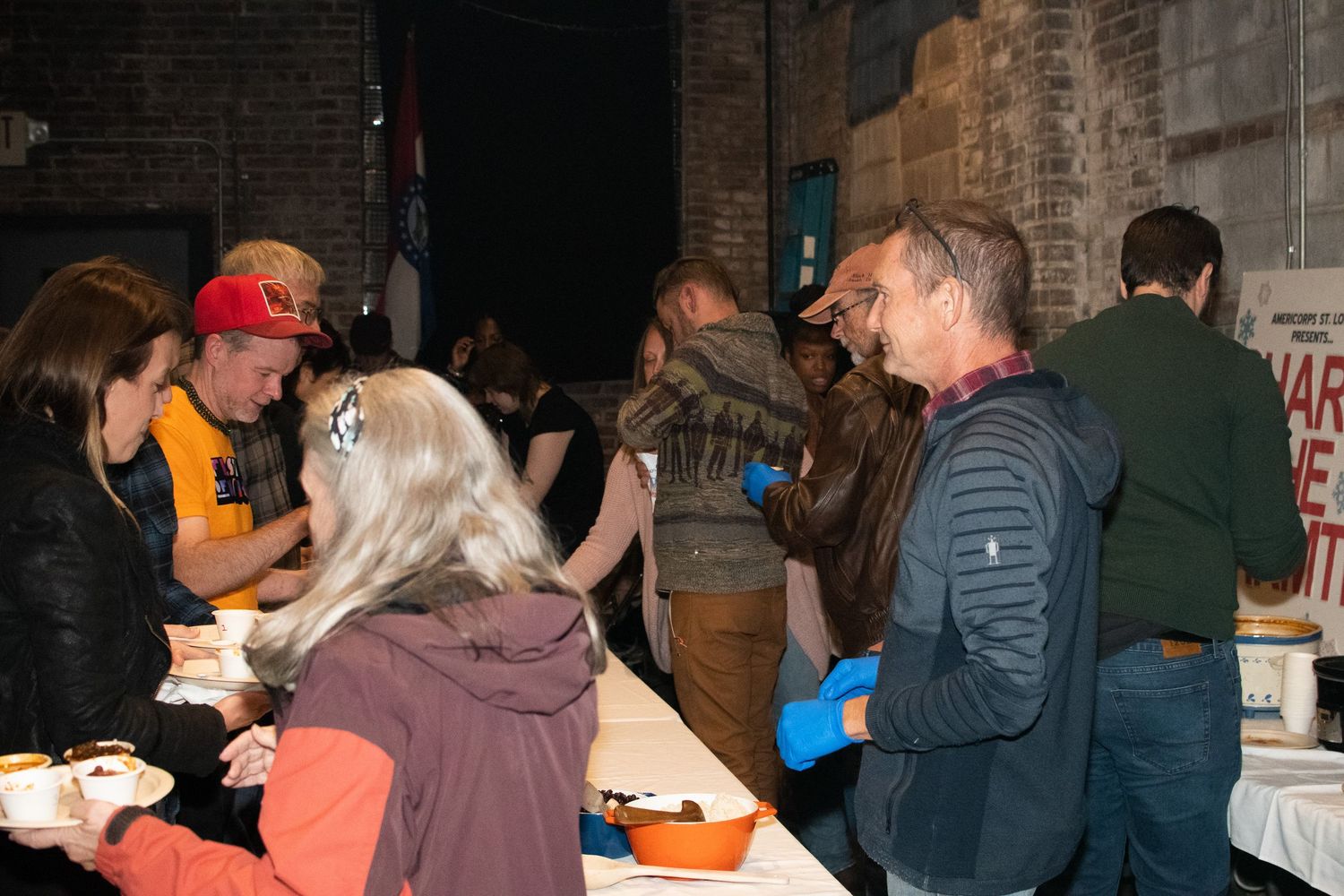 A crowded line of people waiting at a counter or event registration area inside a dimly lit venue.