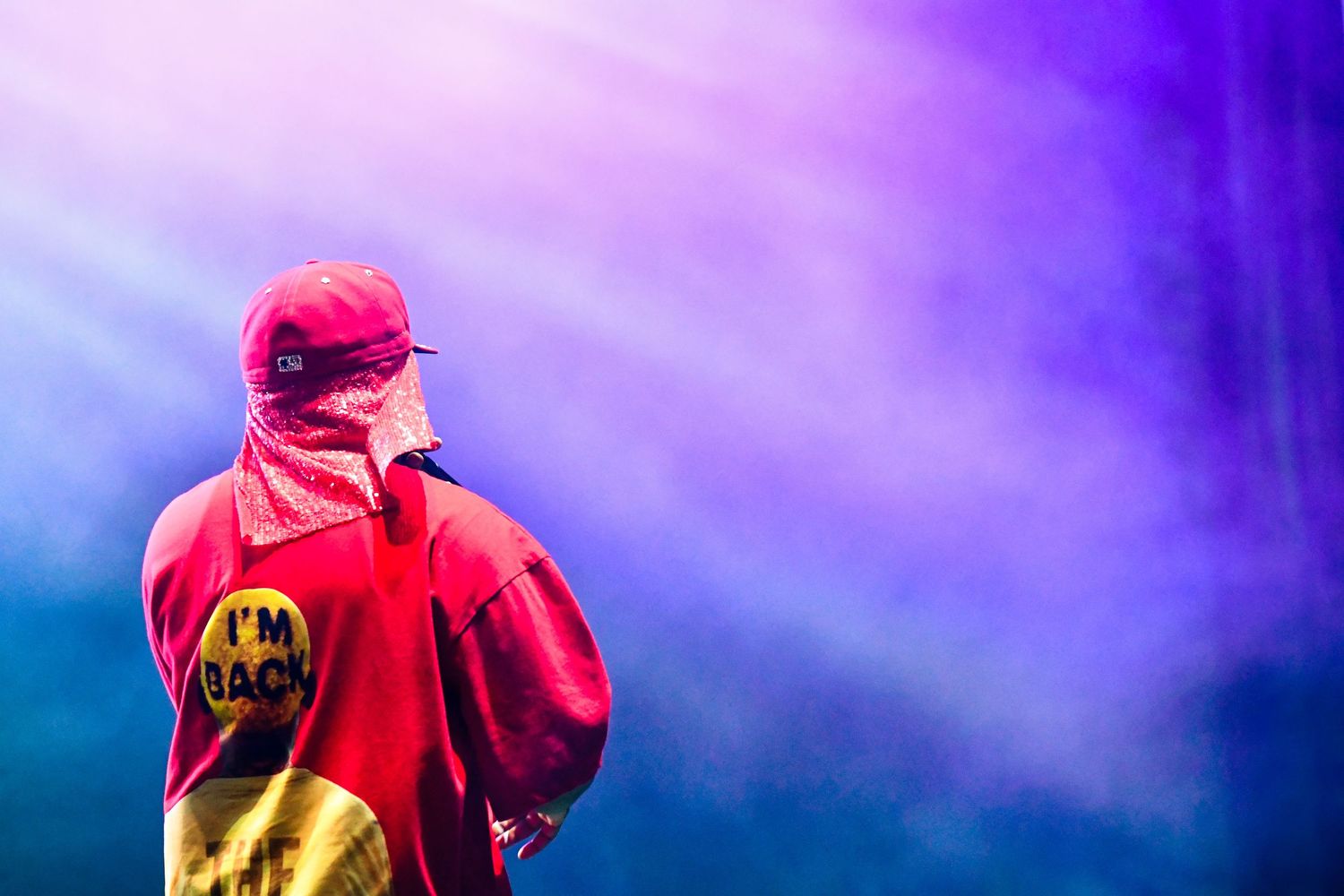 A red-hooded figure stands against a dramatic purple and blue sky with sunbeams streaming through clouds.