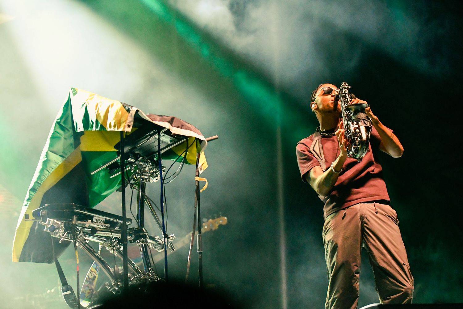 A performer on stage with a microphone and equipment under dramatic green lighting at a concert performance.