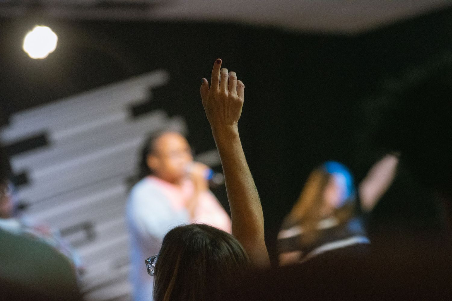 A hand is raised against a dark background with a bright light source visible in the distance.