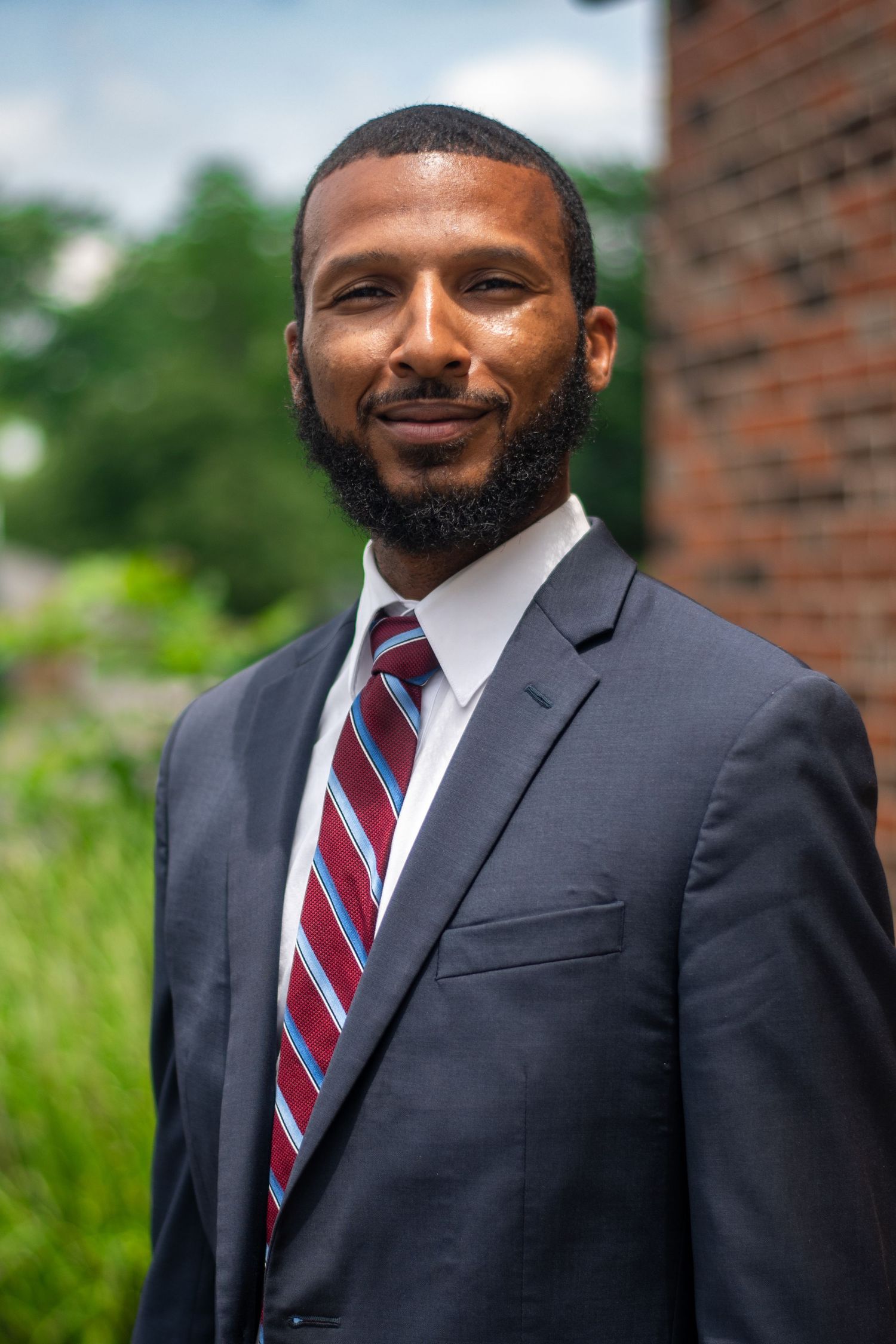 Professional headshots showing confident poses in dark suit and striped tie outdoors.