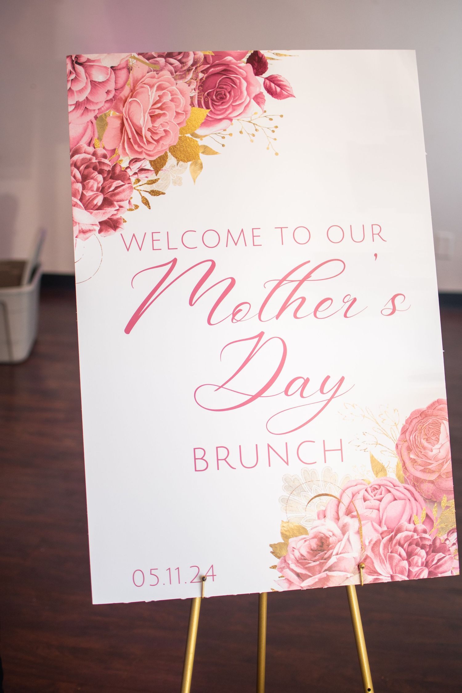 Pink floral wedding brunch signs with elegant calligraphy displayed on gold stands against a dark wooden surface.