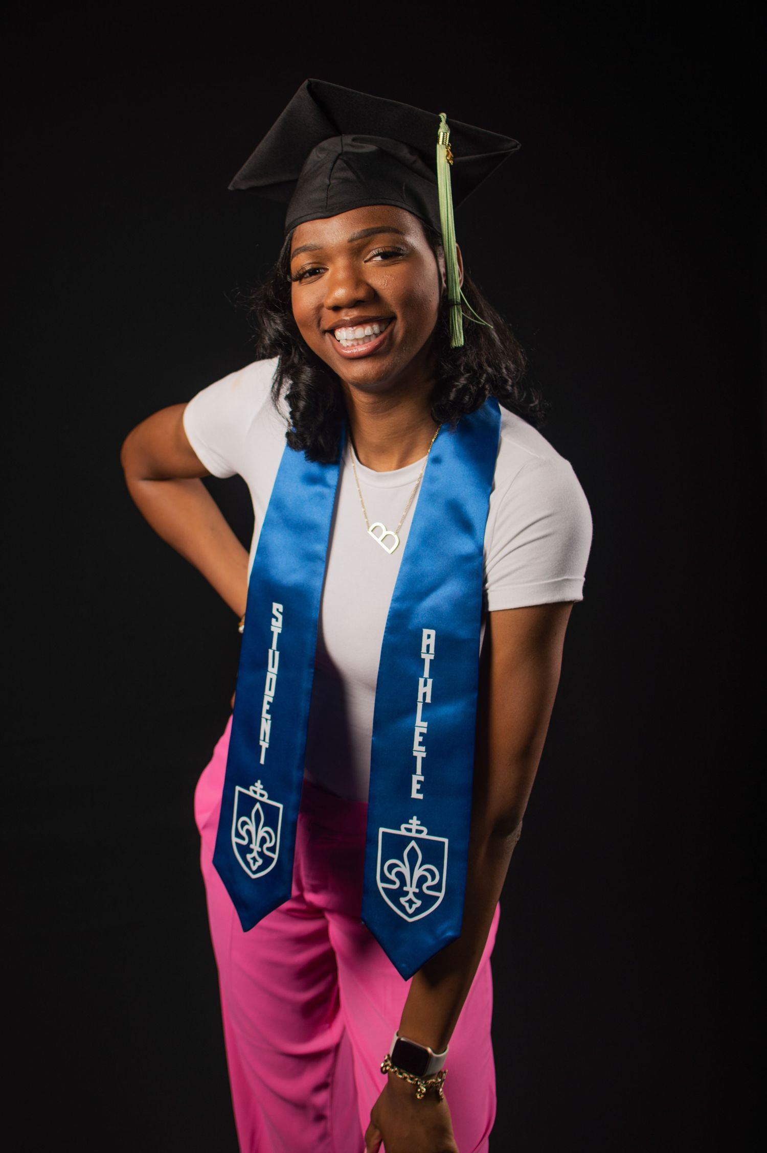 Graduate wearing white shirt and pink skirt poses with blue graduation stole in professional photoshoot.