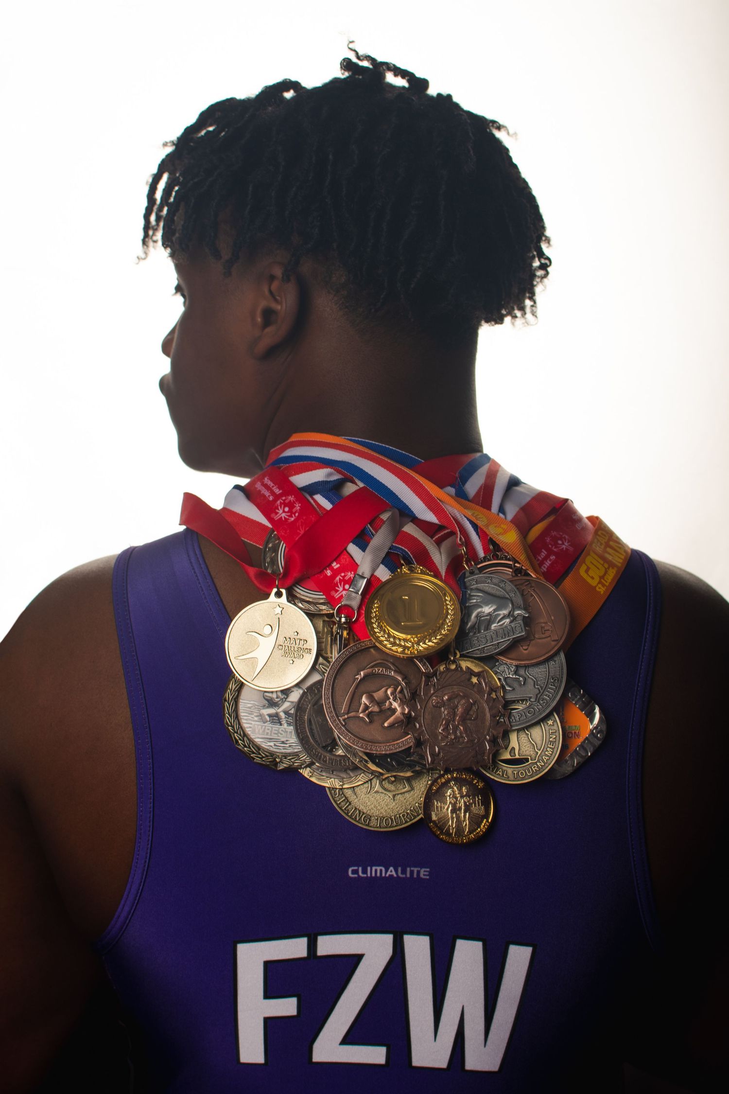 Collection of gold, silver and bronze medals displayed on blue wrestling uniform against white backdrop.