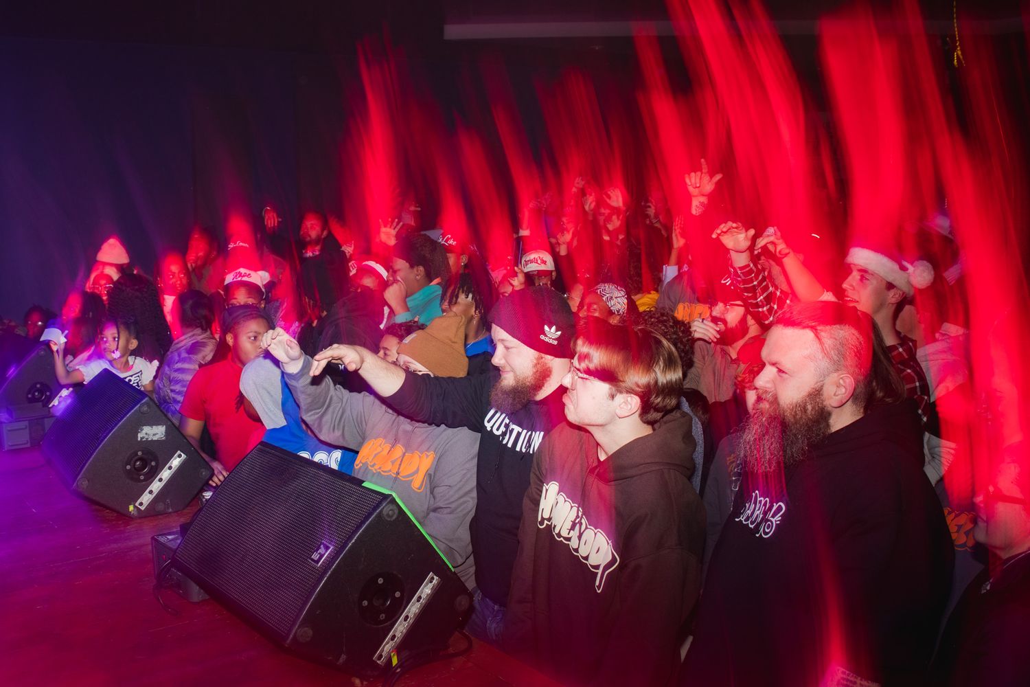 Concert audience members dance and sway in a red-lit venue during a live performance.
