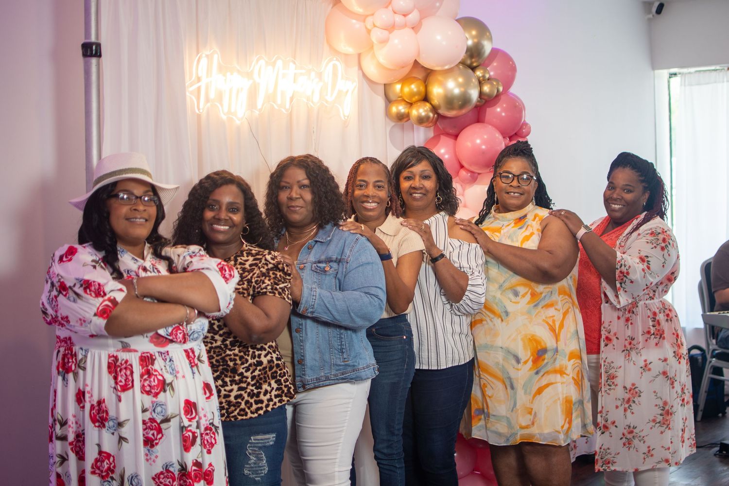 group of black women posing under neon sign with balloons