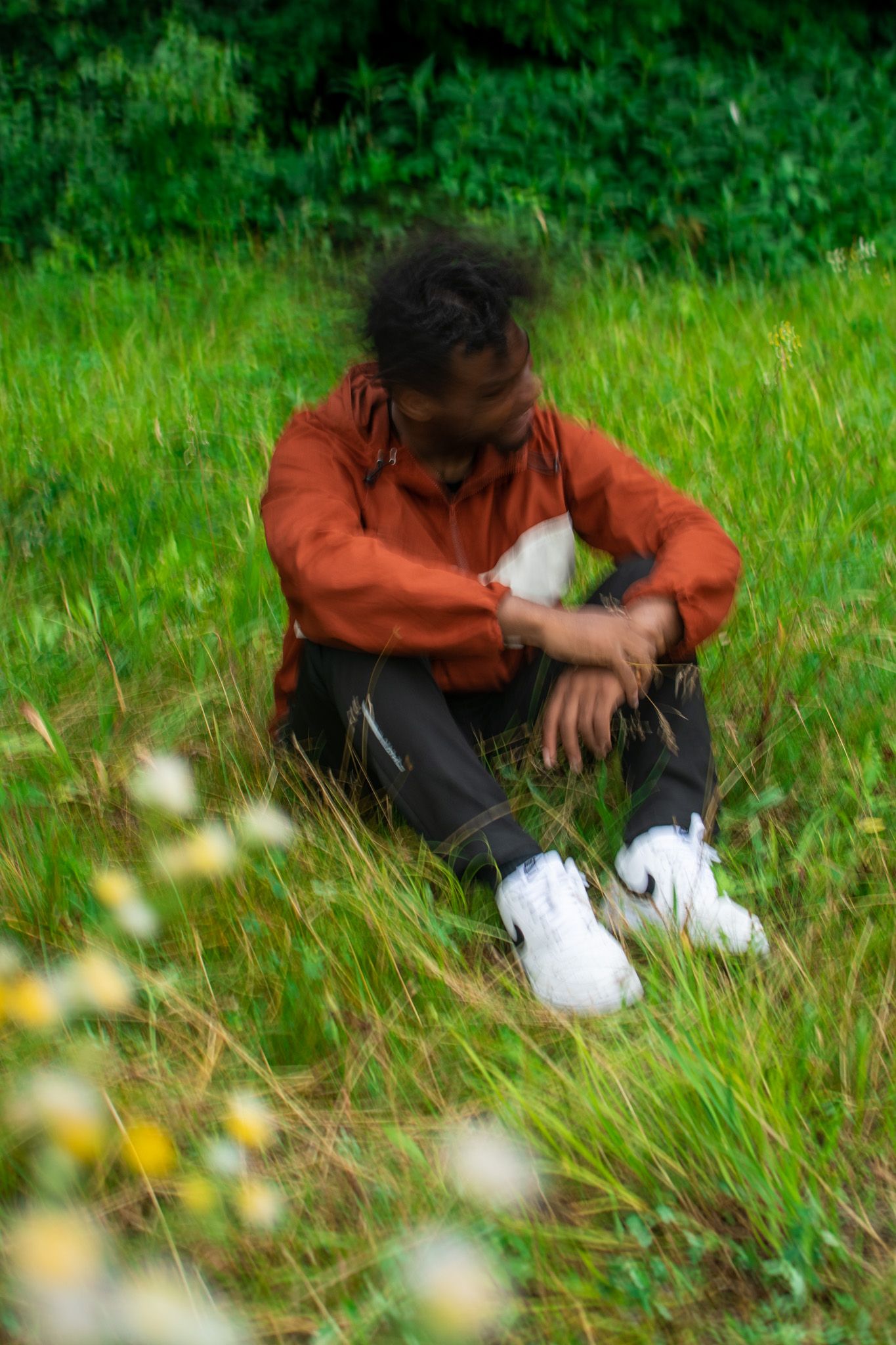 Person in orange jacket sits in green grass field with white flowers in a sequence of artistic motion shots.