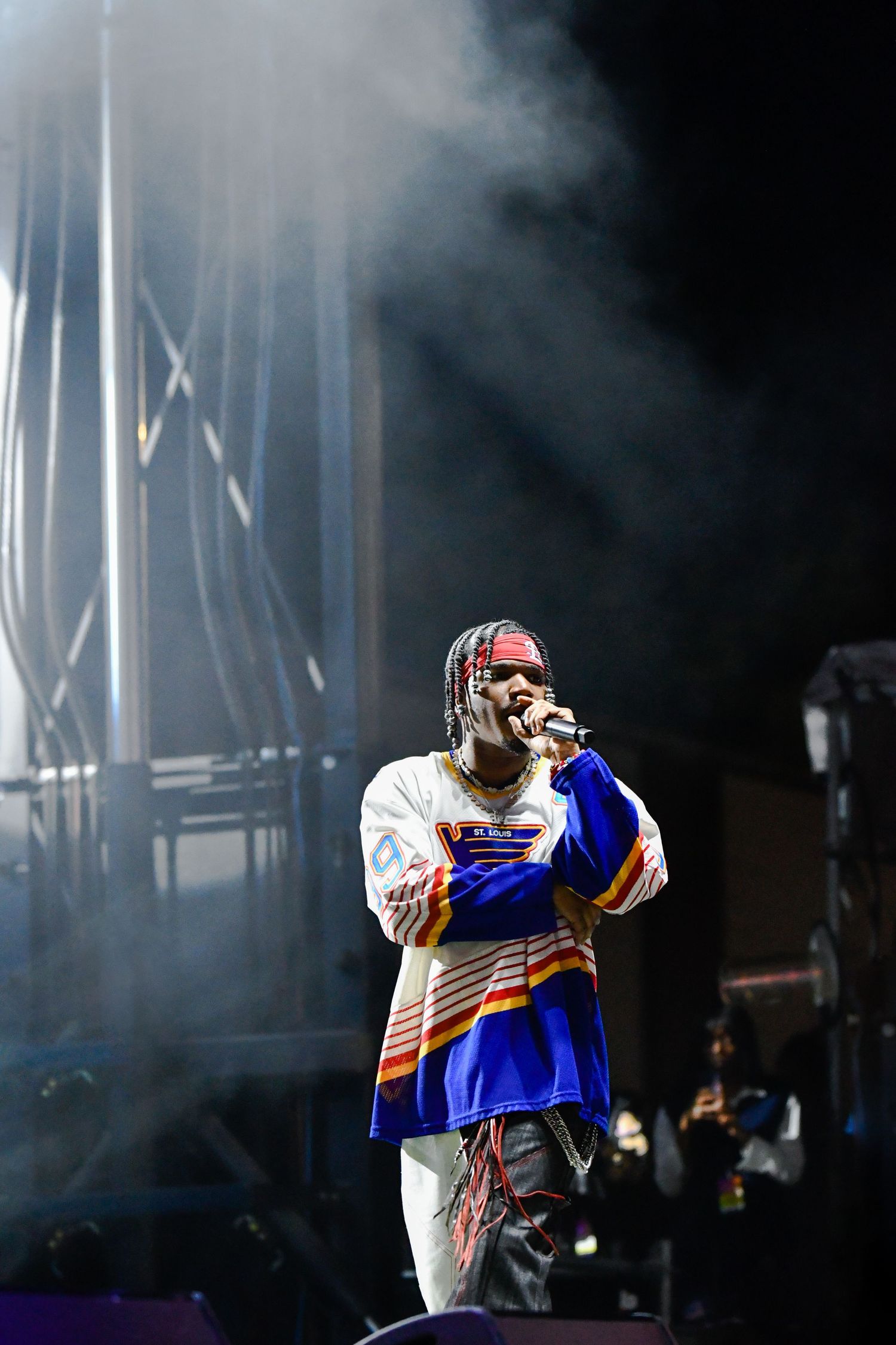 Performer in white and blue outfit dances energetically on dark stage with dramatic lighting and smoke effects.