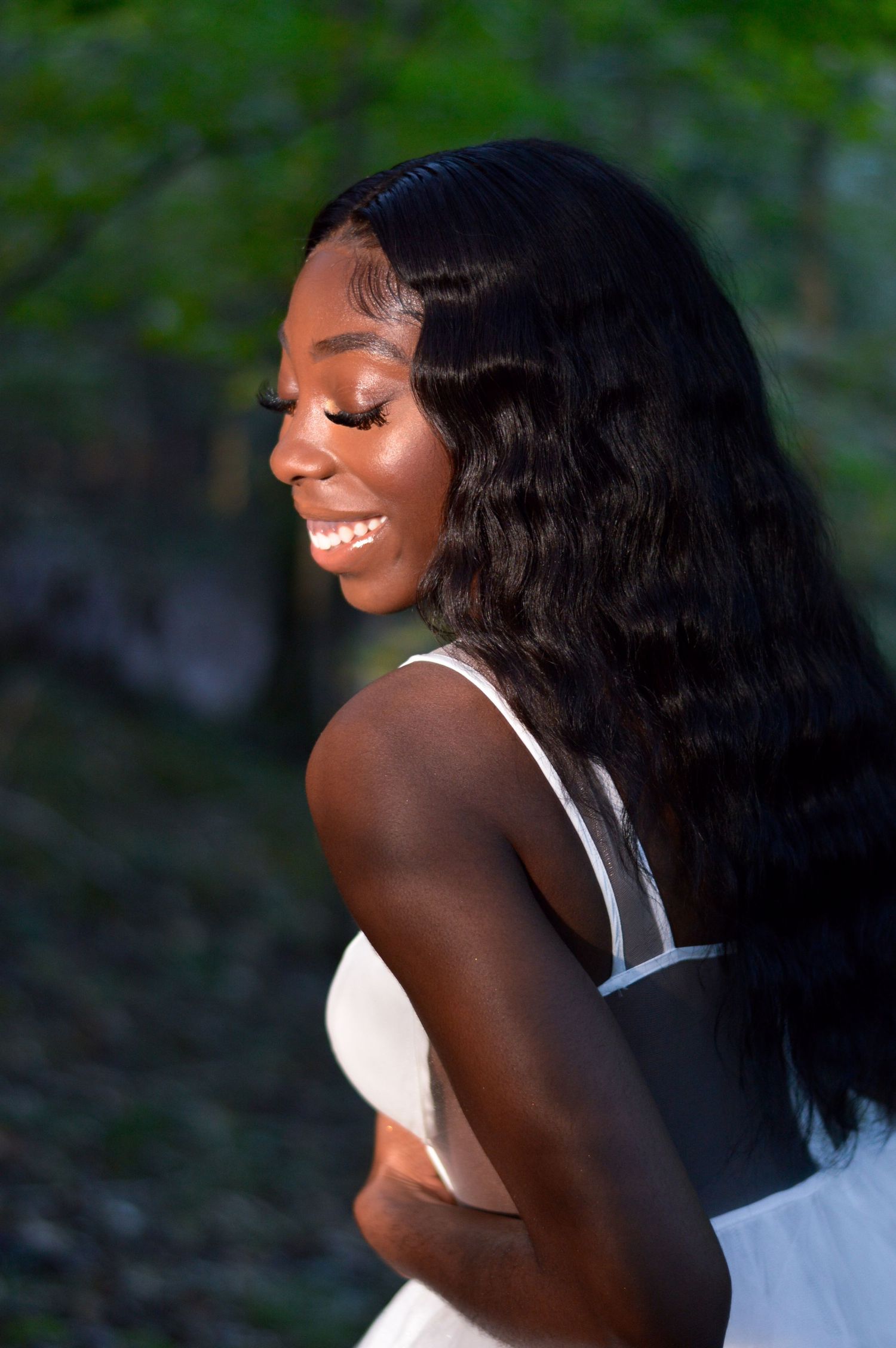 A side profile portrait showing a bright smile and long flowing dark hair against a blurred natural background.