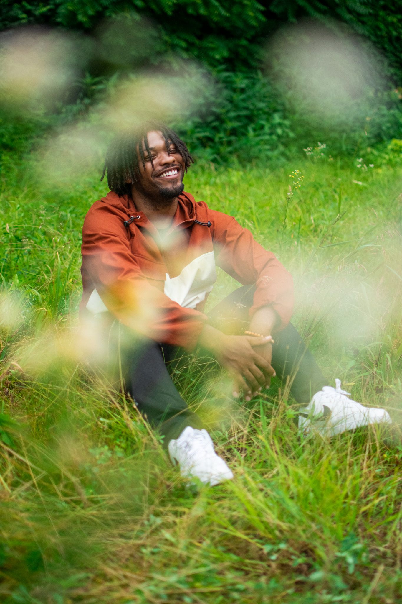 Someone in a rust-colored sweater sits in tall grass with a dreamy, soft-focus effect in the foreground.
