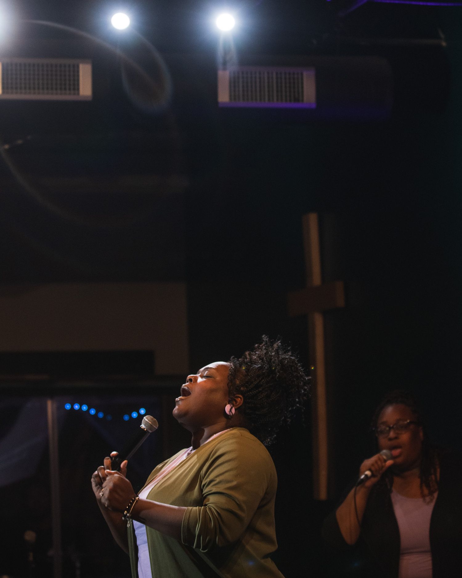 A performer sings passionately on stage under dramatic spotlights during a concert performance.