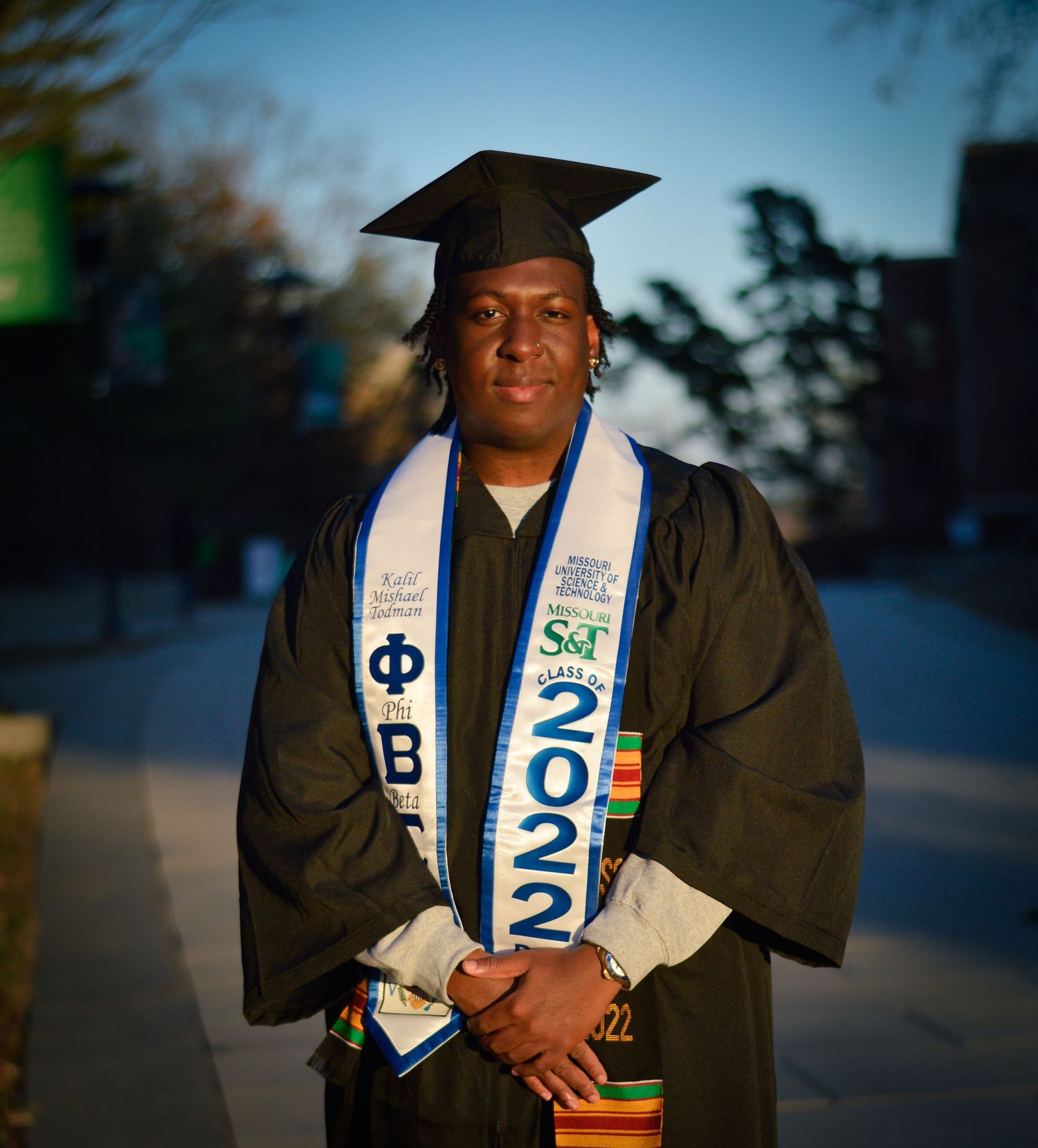 Outdoor graduation photo showing academic regalia and class of 2022 stole at sunset.