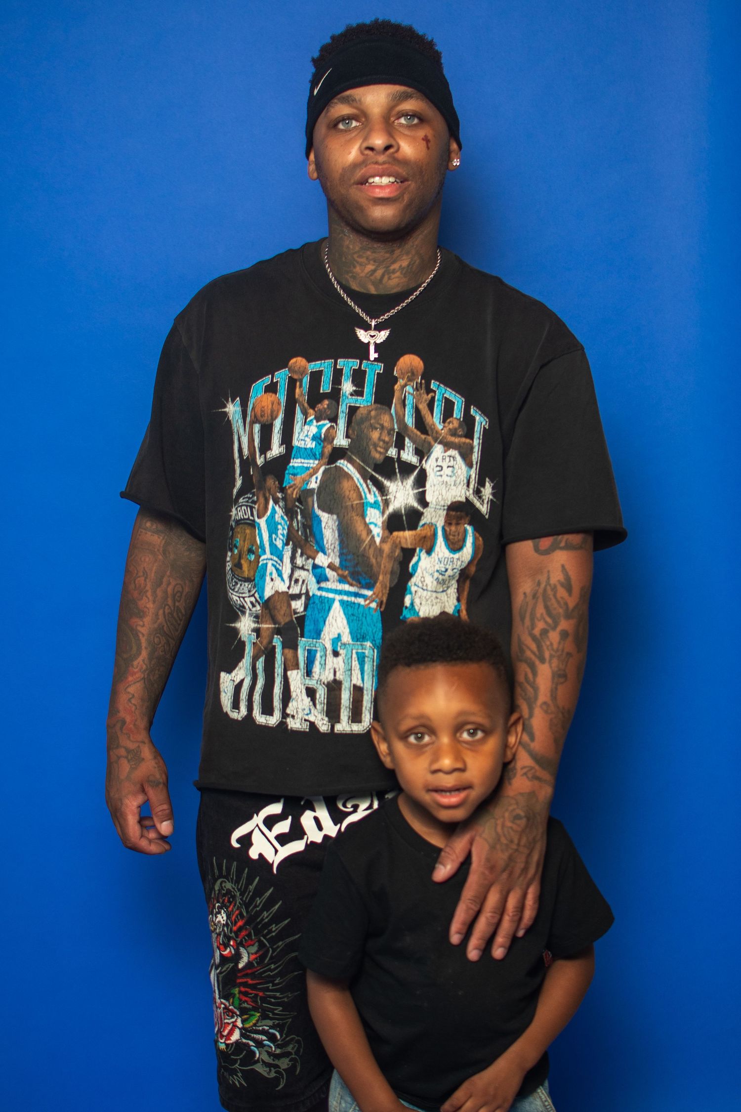 Studio portrait series against blue backdrop showing parent and child wearing black t-shirts and sharing tender moments together.