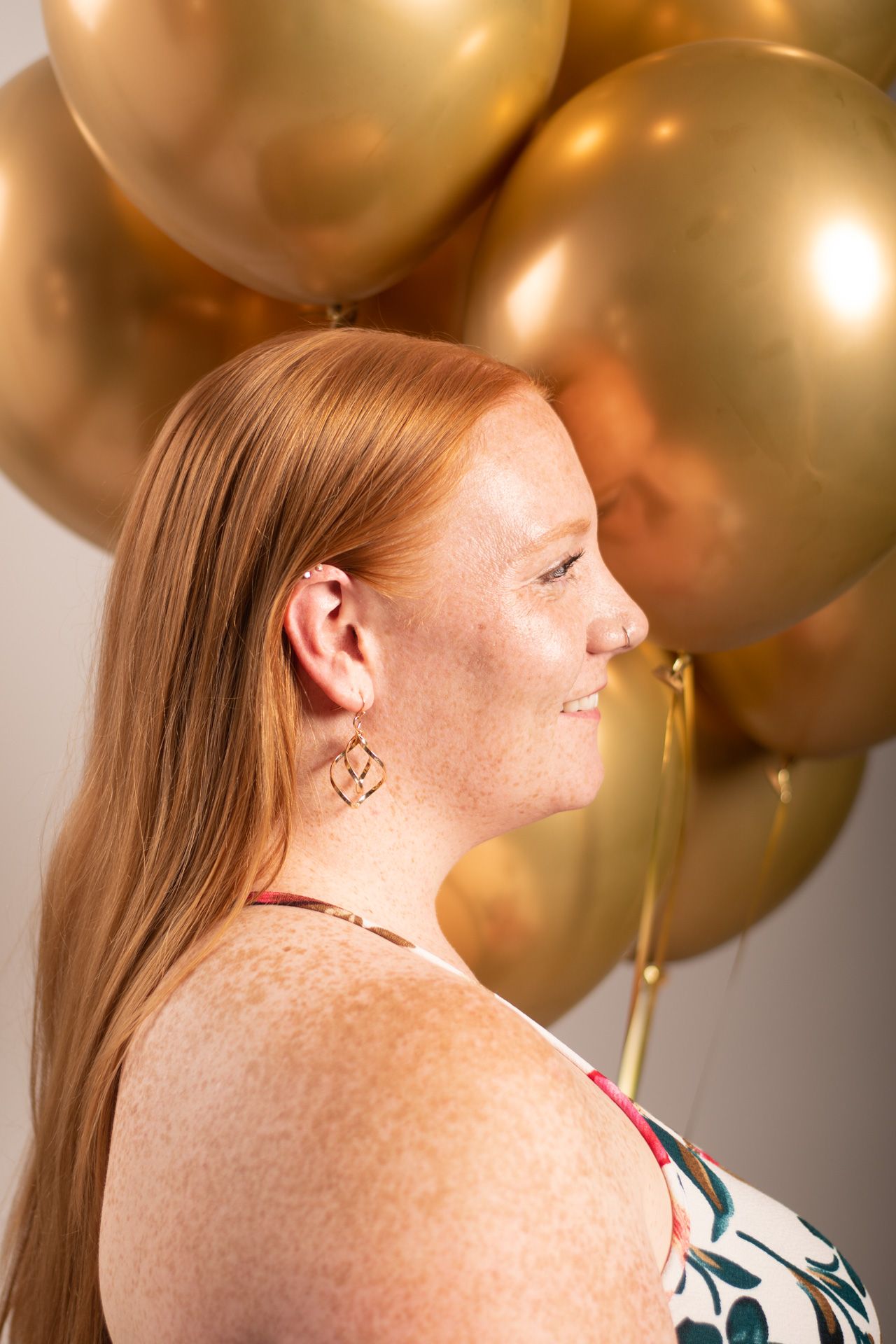 Side profile portrait against golden balloons background showing freckled skin and blonde hair.