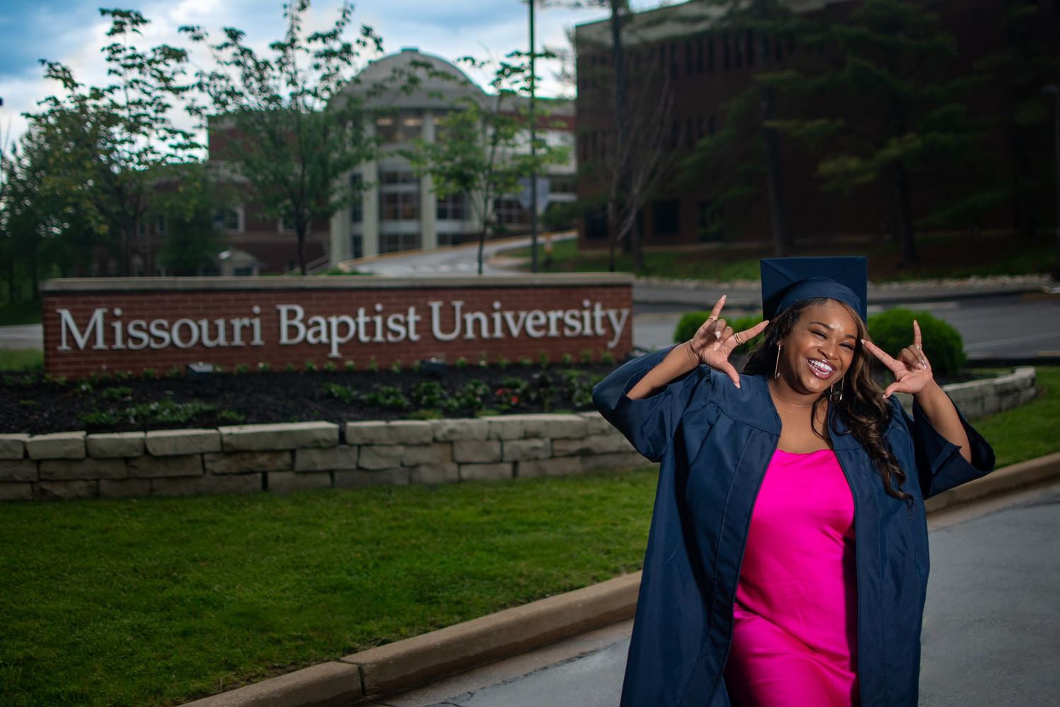 Celebratory graduation photo at Missouri Baptist University entrance sign.