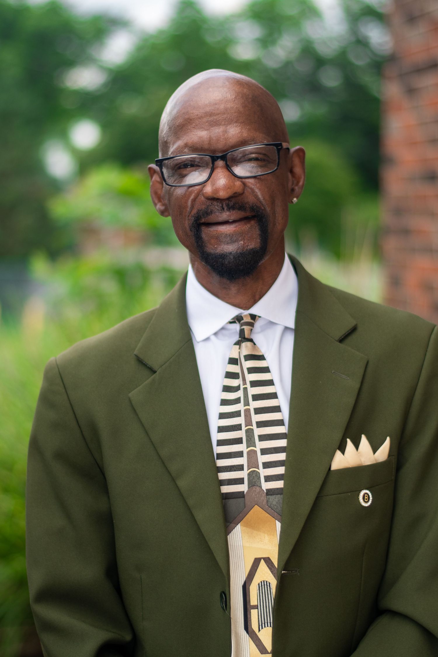 A series of headshots showing a person wearing an olive green suit with a striped tie and pocket square against a blurred background.