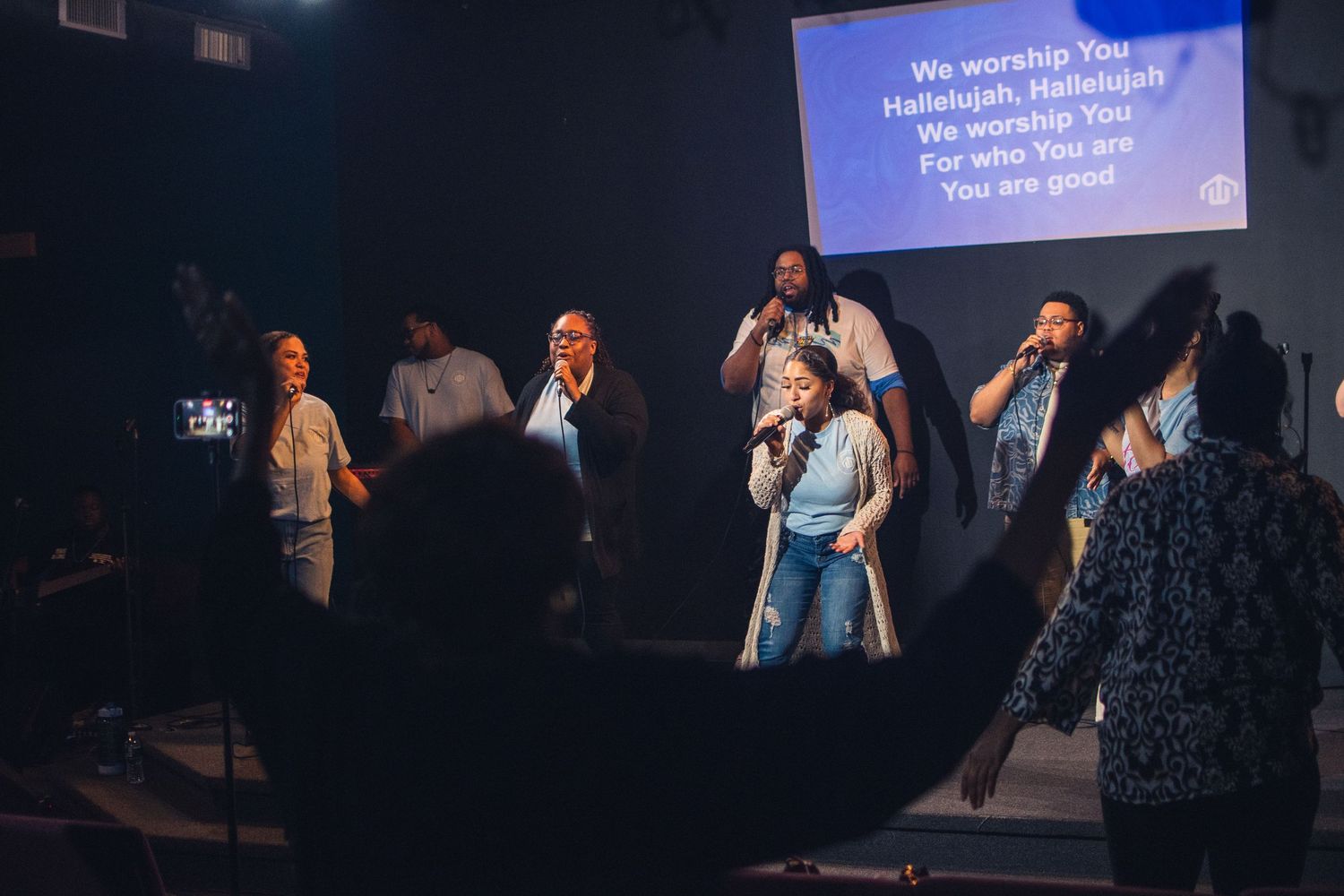 Church worship service with projected lyrics and musicians performing on a dark stage with blue lighting.