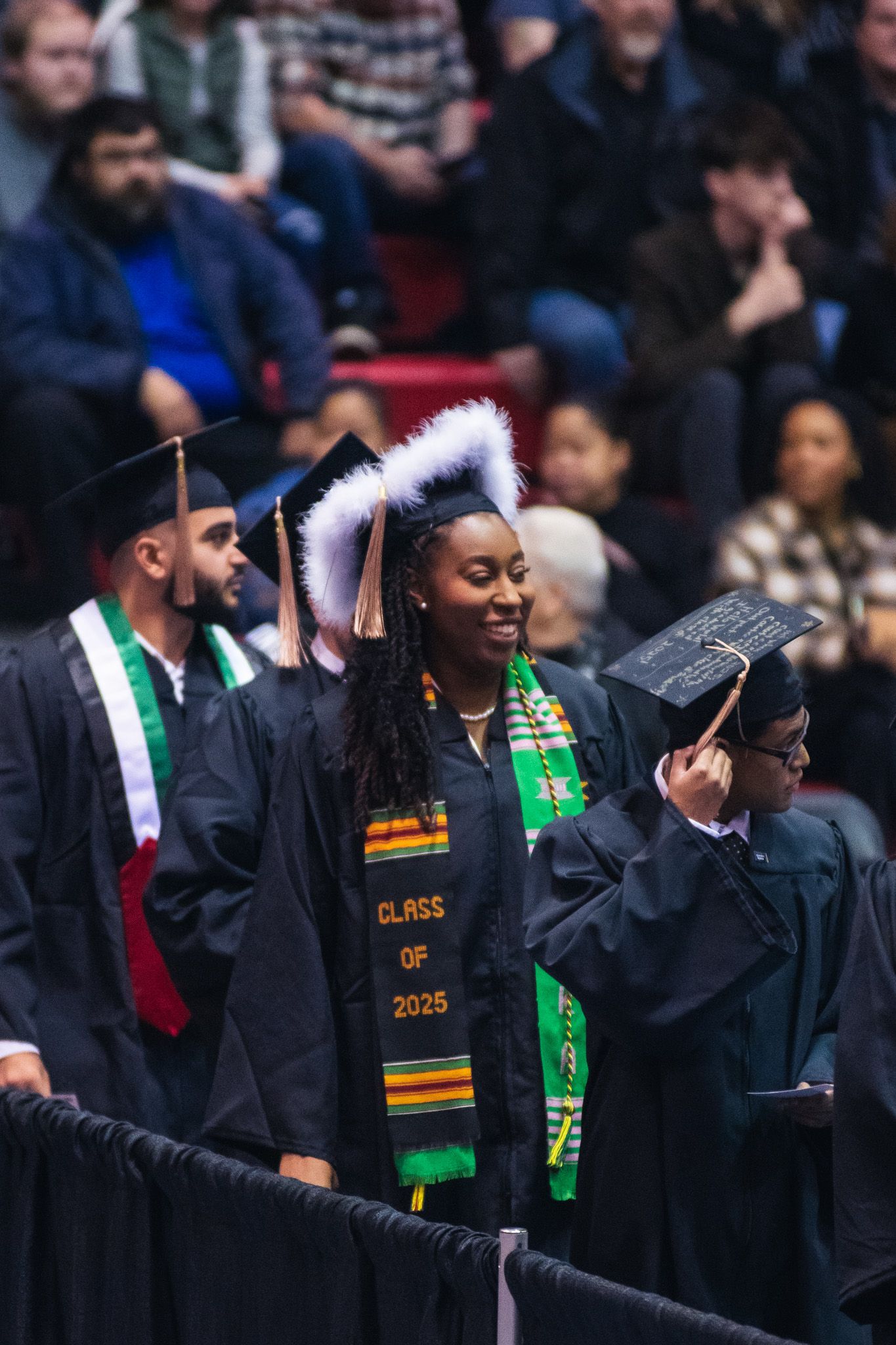Graduates in black caps and gowns with colorful stoles celebrate during commencement ceremony.