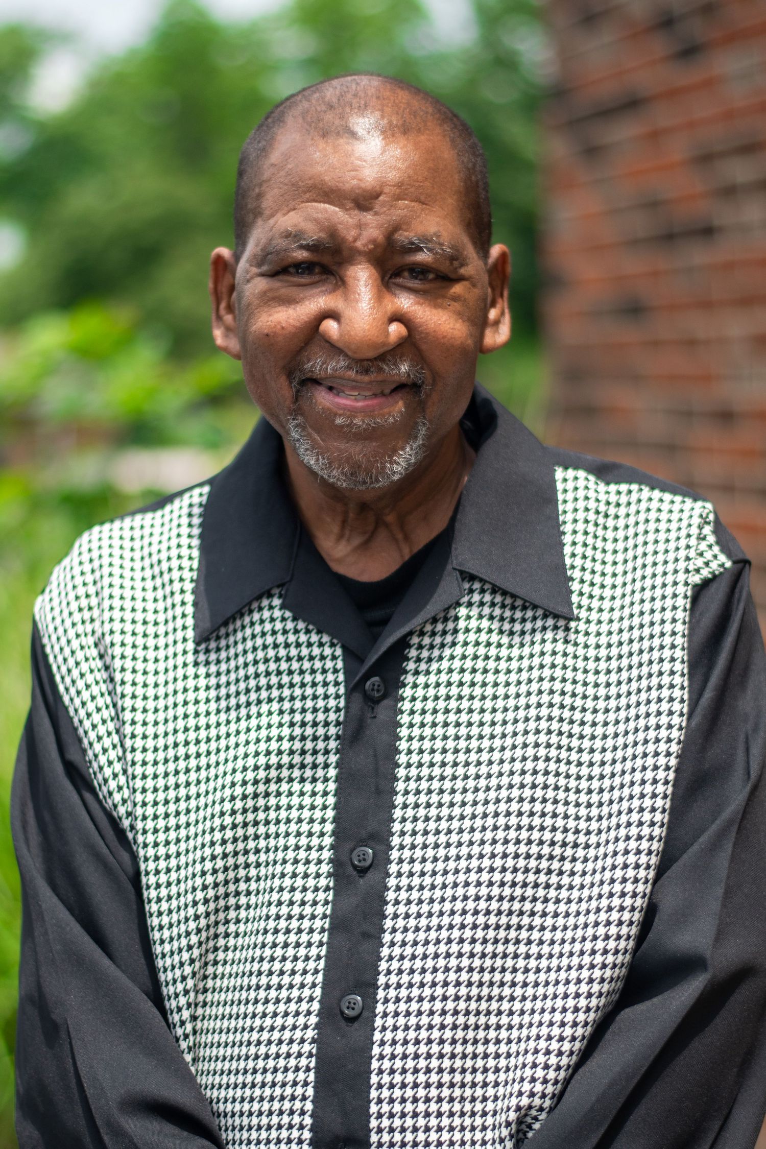 Person wearing a black and white houndstooth vest with black shirt smiling warmly in an outdoor setting.