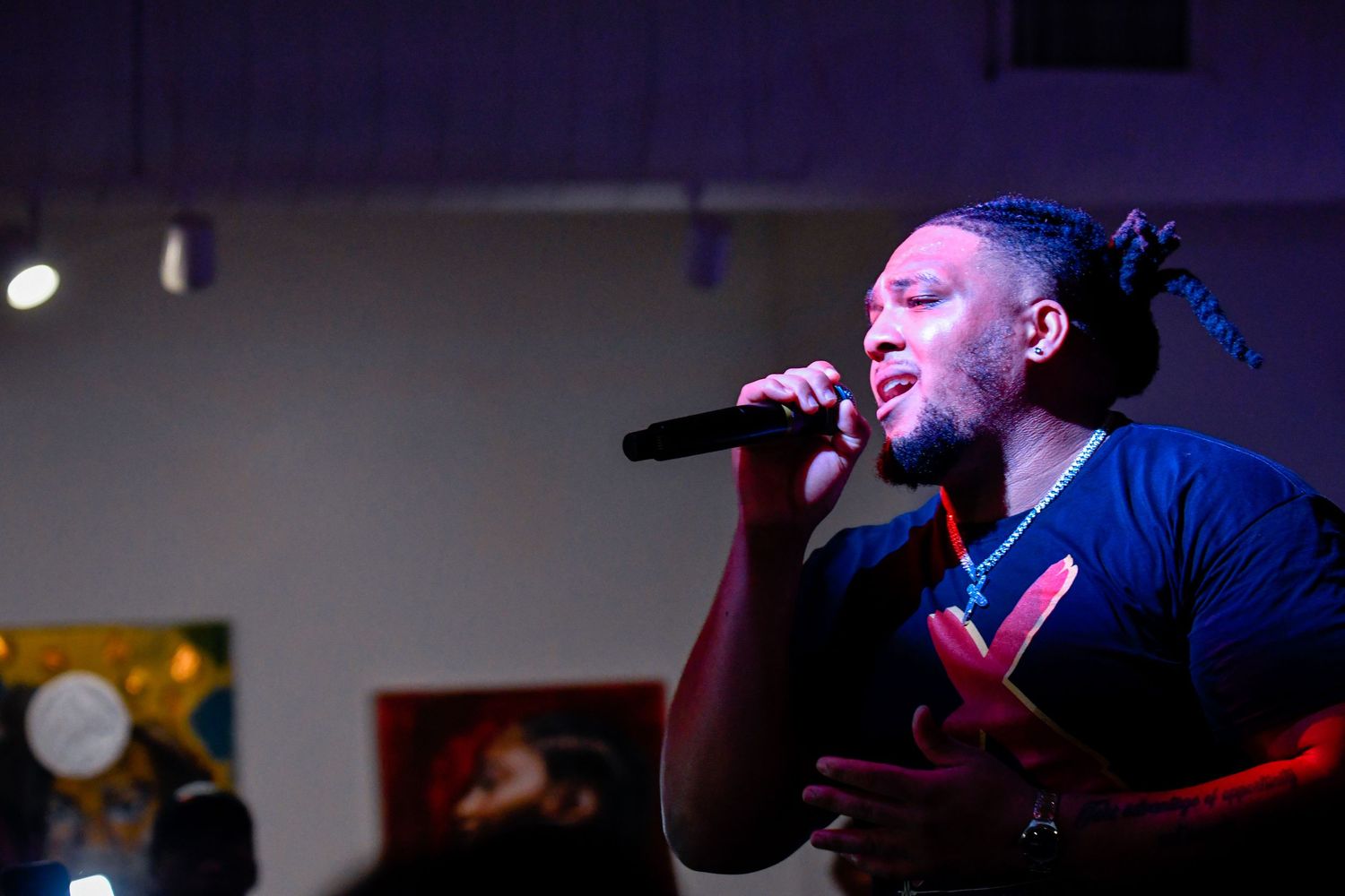 A performer passionately sings into a microphone on stage under dramatic purple and blue lighting.