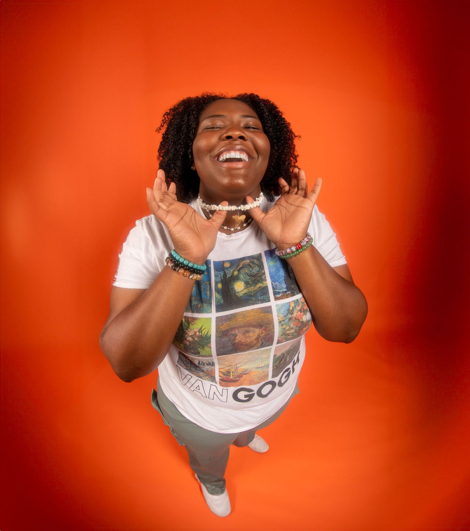 Joyful person wearing a graphic t-shirt and bracelets poses expressively against a vibrant orange background.