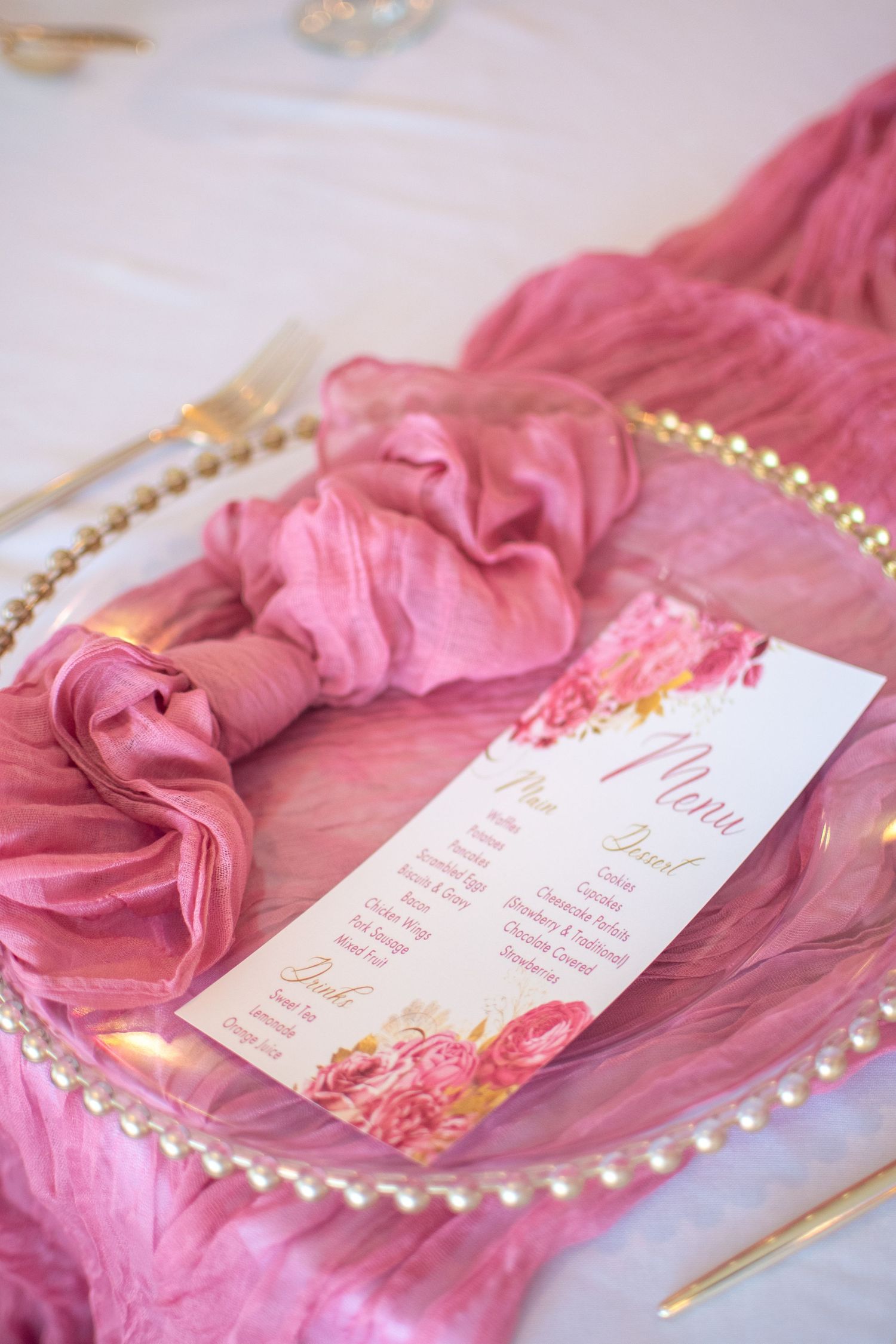 Pink silk fabric with gold trim and elegant wedding invitation cards arranged in a romantic styled layout.