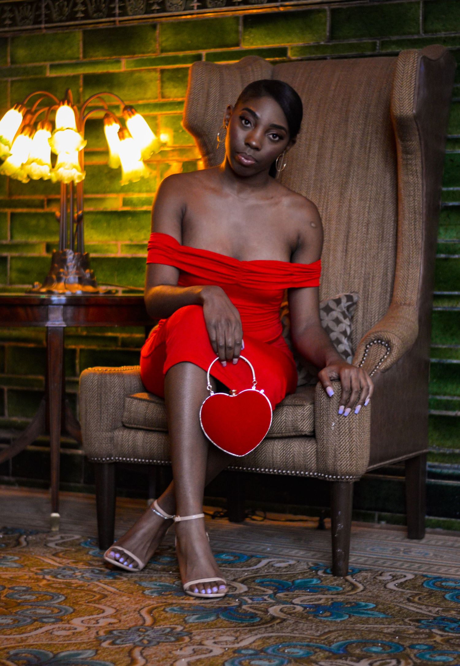 A figure in a red off-shoulder dress sits elegantly on a patterned couch holding a heart-shaped accessory.