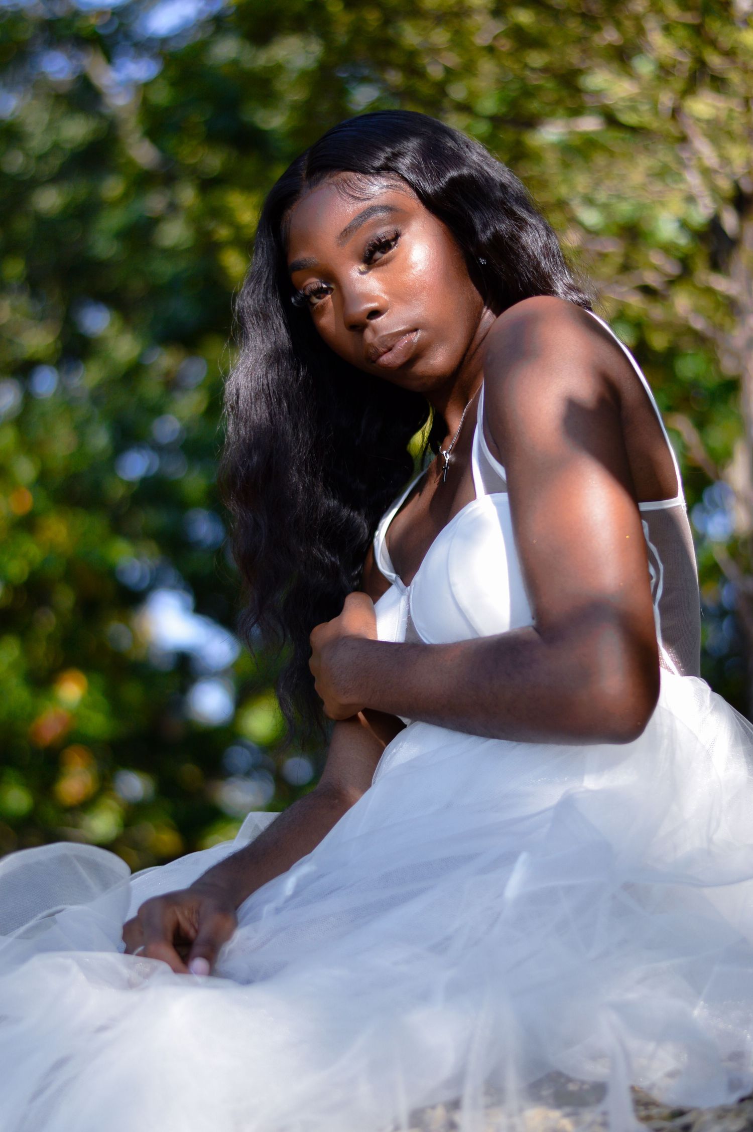 A graceful figure in a white dress poses elegantly against a natural outdoor backdrop with soft bokeh lighting.