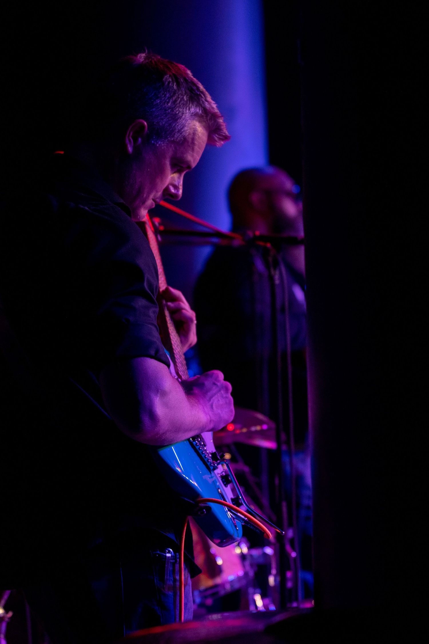 Musician performs on stage illuminated by dramatic blue and purple lighting during a concert performance.
