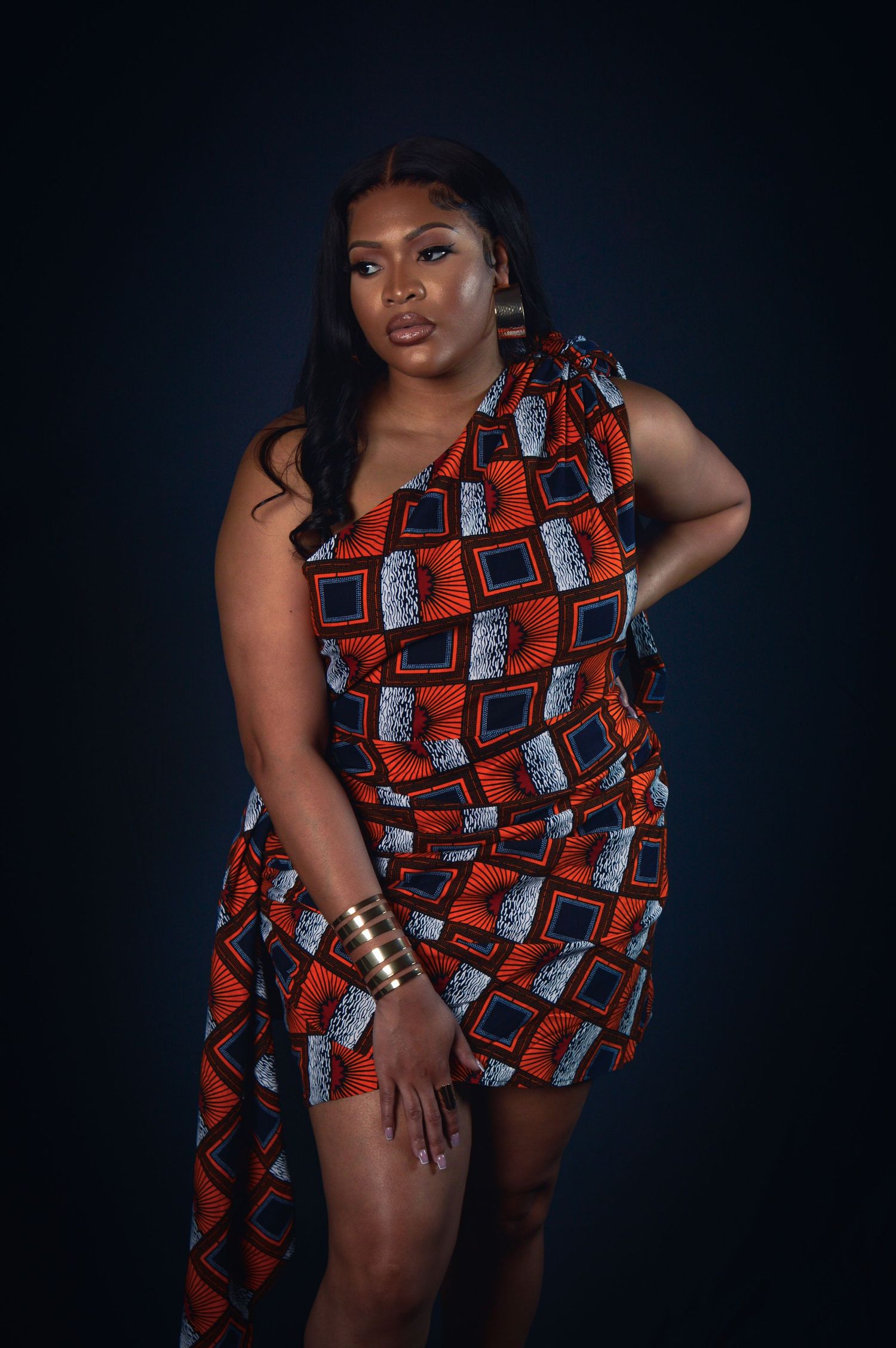 Fashion model poses in vibrant orange and black geometric print dress against dark background in multiple shots.