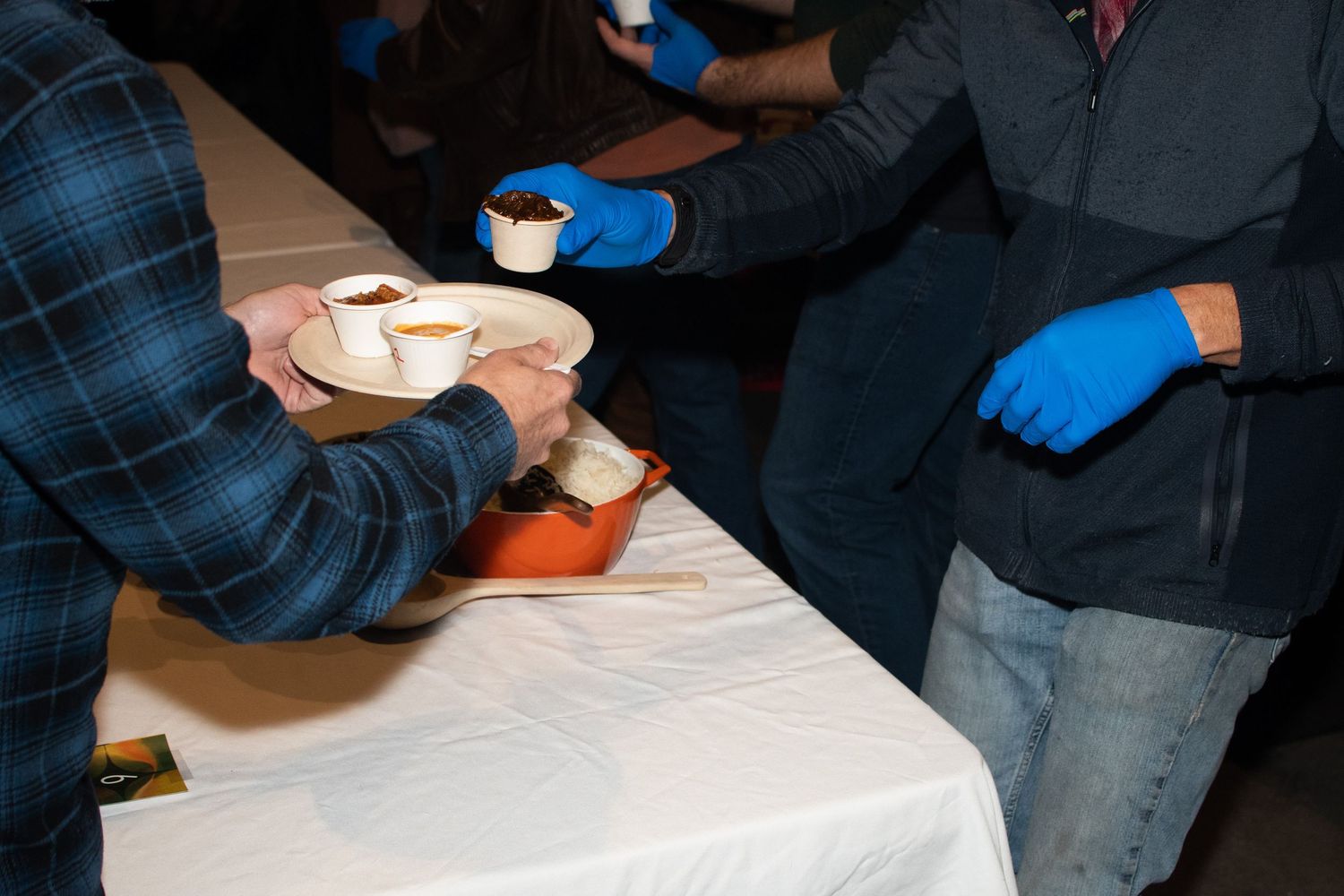 People wearing blue gloves handle items on a white tablecloth during an indoor event.