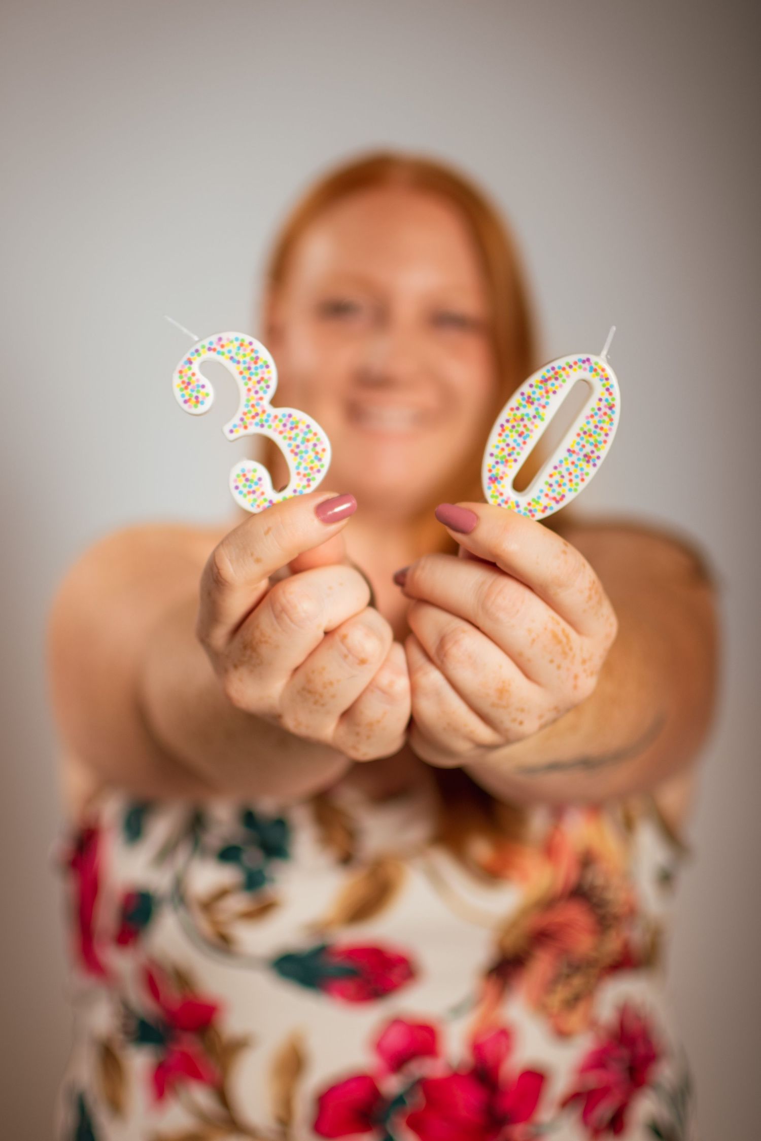 Person holding sparkly number 30 decorative birthday candles while wearing a floral patterned dress.