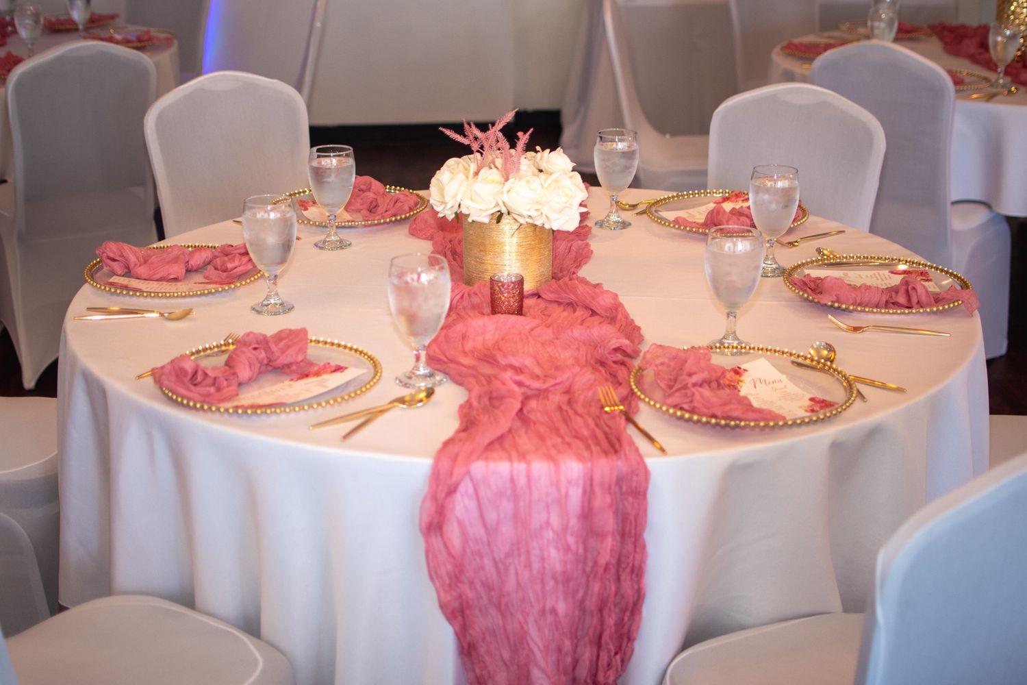 Elegant wedding reception table with white tablecloth, pink runner, glowing centerpiece and formal place settings.